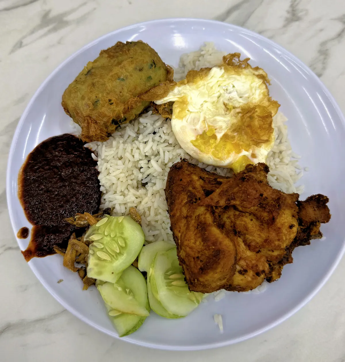 A Wanjo nasi lemak plate with fried chicken, a fried egg, begedil, dark sweet sambal, and cucumber