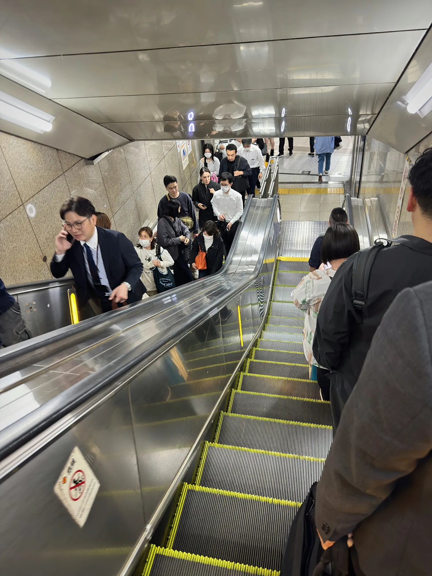 Looking down a busy station escalator at rush hour in Osaka, with commuters riding single file on one side.