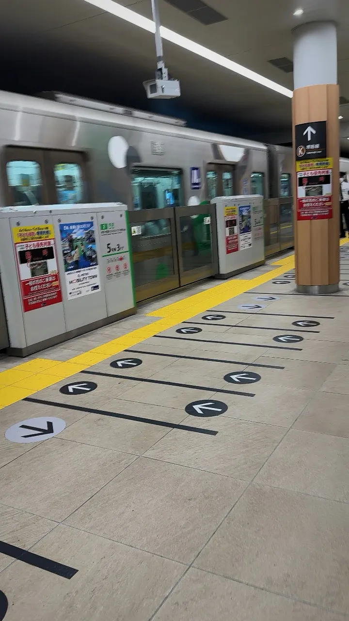 Floor lines and arrows marking the boarding queues beside the platform doors, with a silver subway train waiting behind them in Osaka.