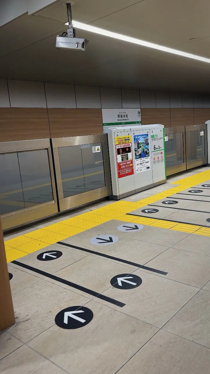 Black boarding lines and arrows on the floor of an Osaka subway platform, marking where to queue on each side of the platform doors.