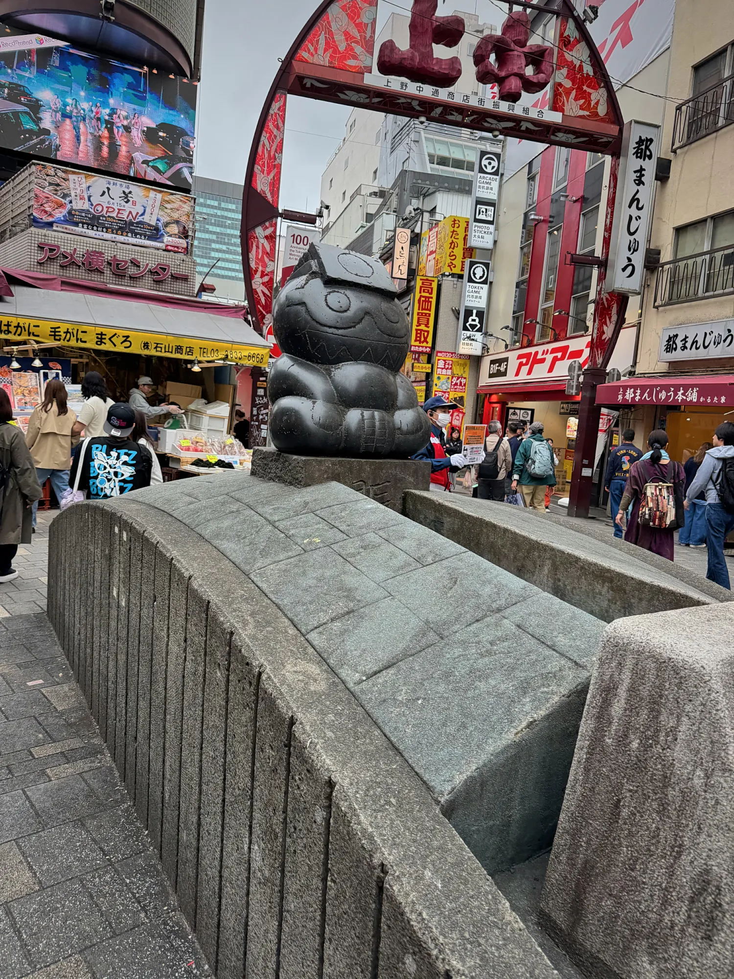 The cat statue at the entrance to Ameyoko market street in Ueno, Tokyo, under the red arch sign.