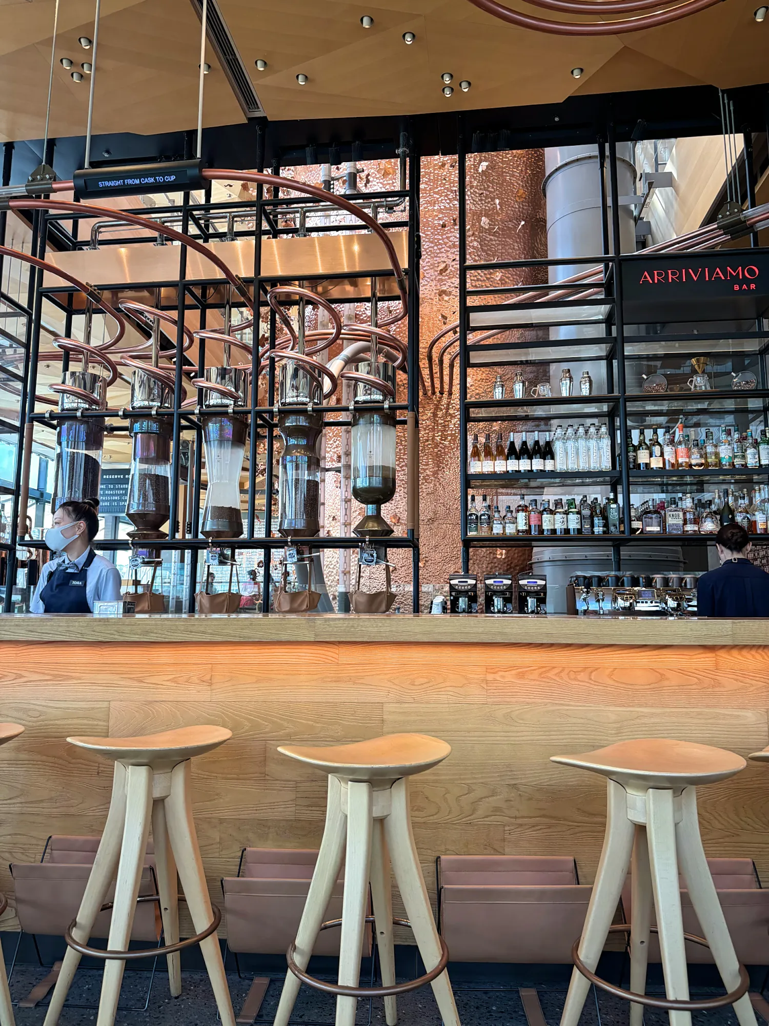 The Arriviamo cocktail bar counter with tall stools, copper brewing pipes, and shelves of spirits at Starbucks Reserve Roastery Tokyo.