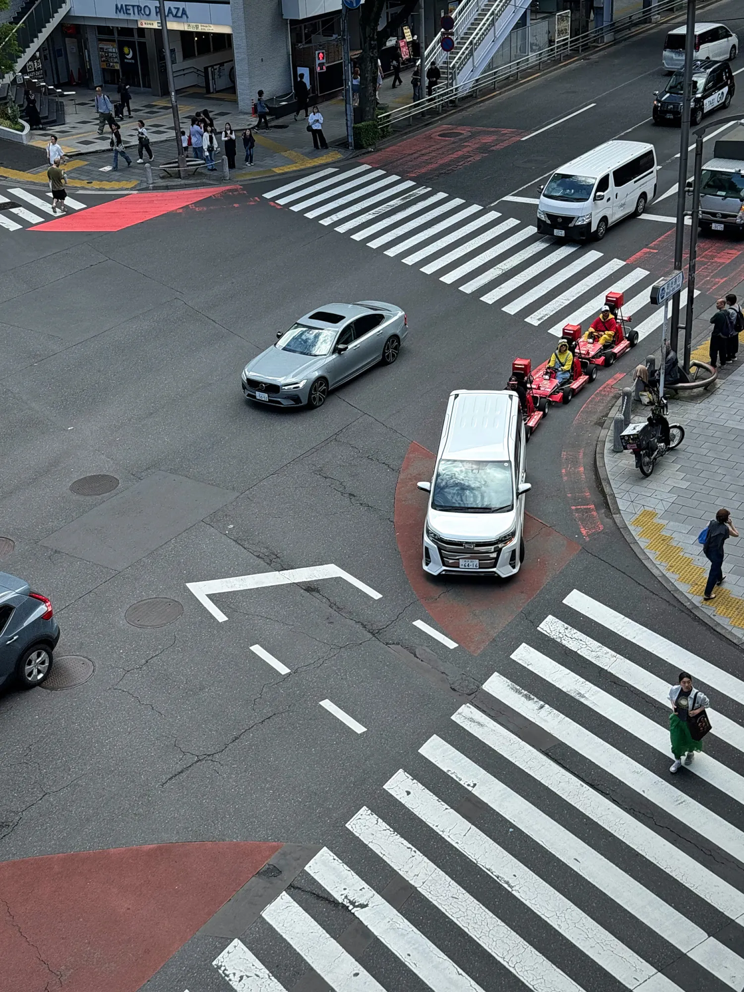 A Shinjuku intersection seen from above, with striped crosswalks and cars waiting at the light.