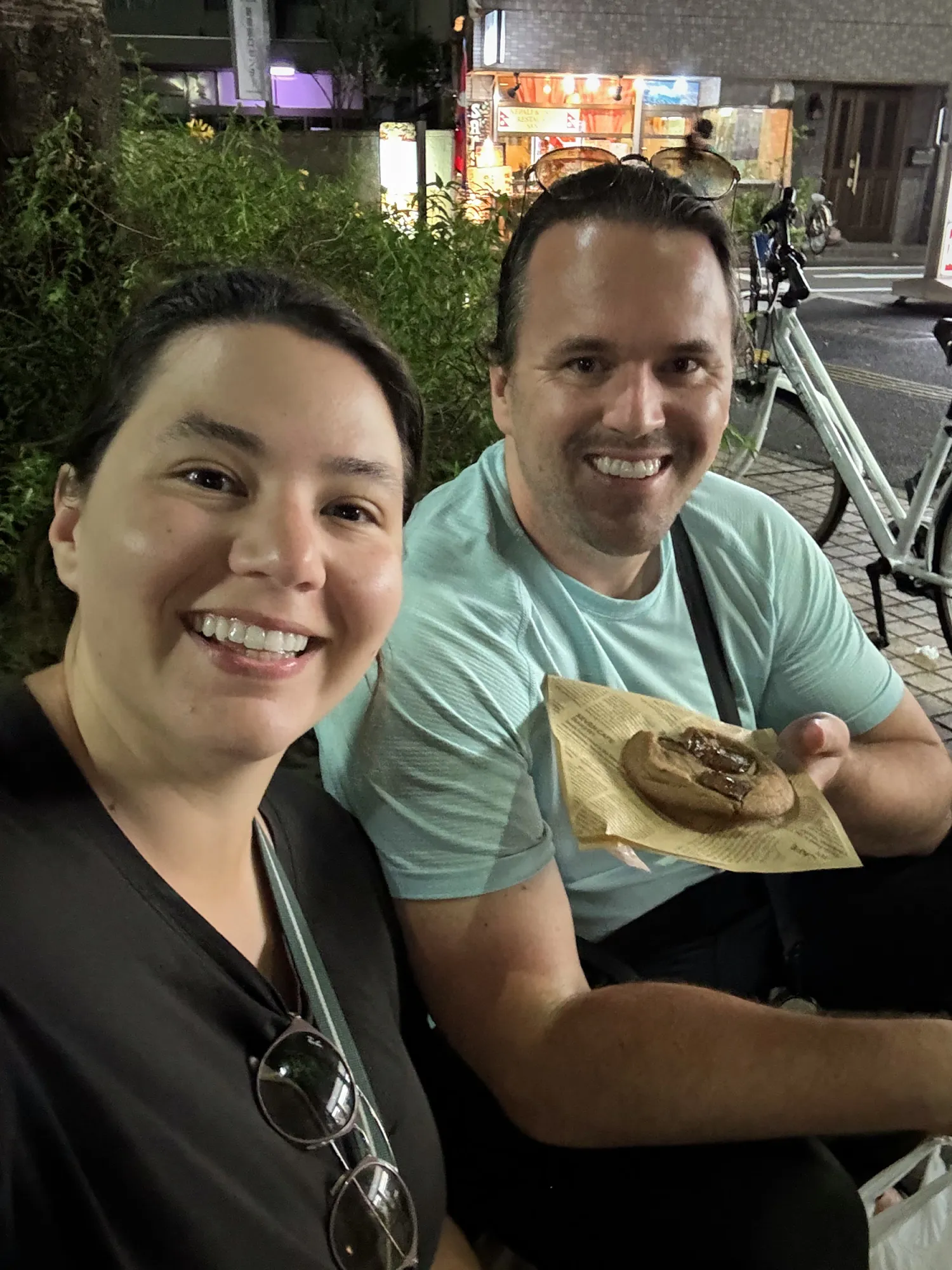 Bernie and Cream smiling in a night selfie outside a 7-Eleven in Tokyo, holding a cookie.