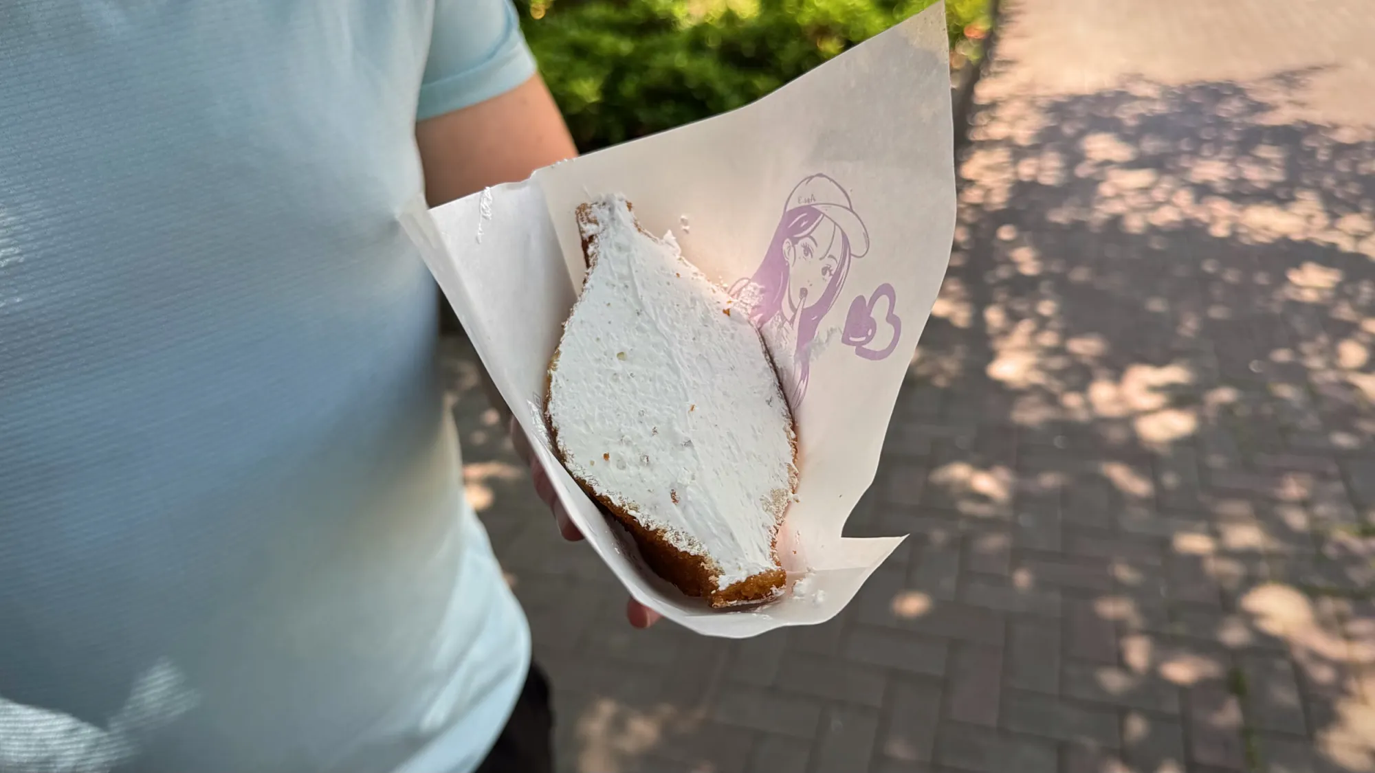 A whipped cream fried sandwich in its Age.3 paper sleeve, held over a sunny sidewalk in Ginza.