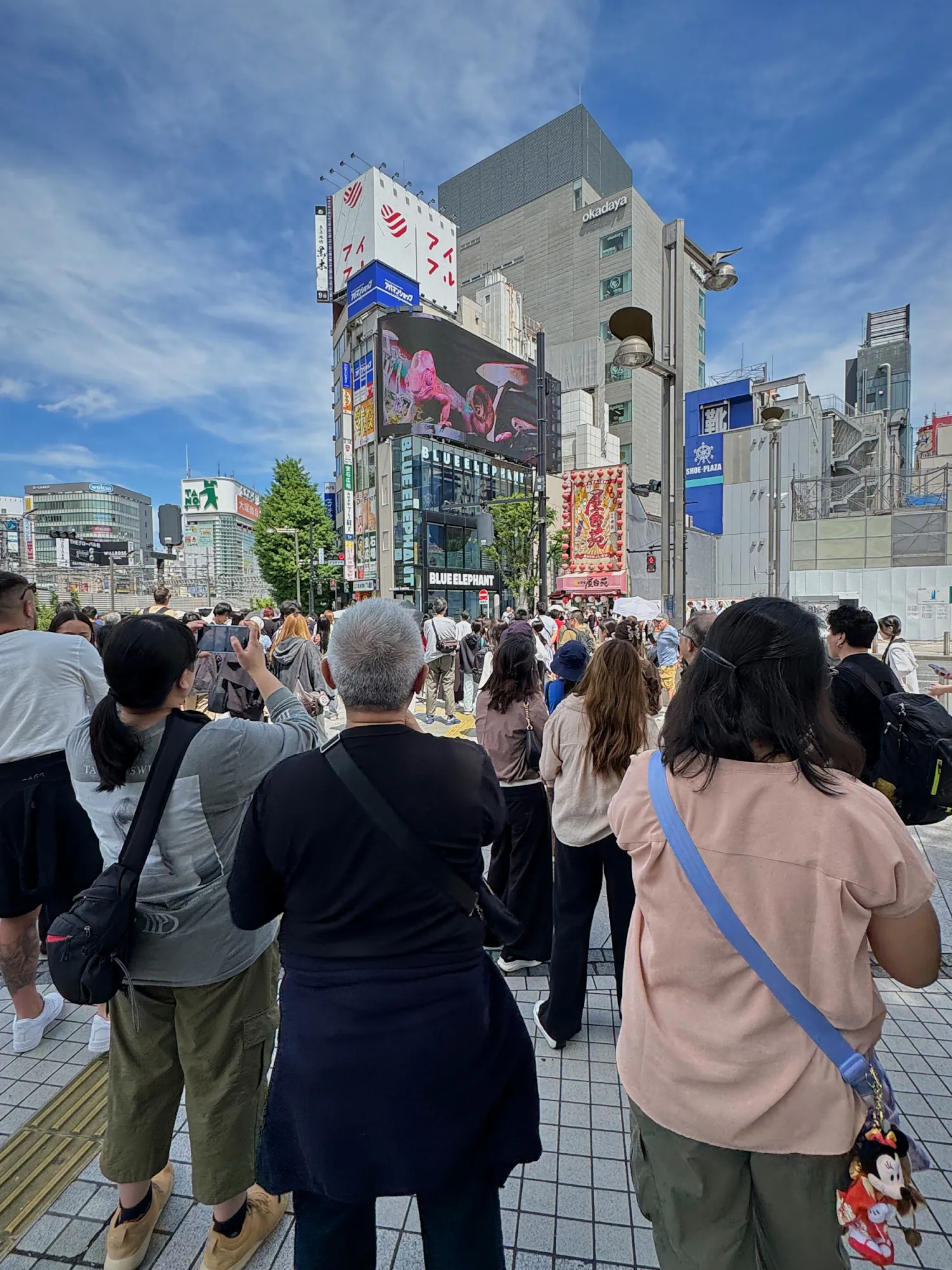 A crowd on the sidewalk outside Shinjuku Station's East Exit watching the giant 3D billboard on the corner building, Tokyo.