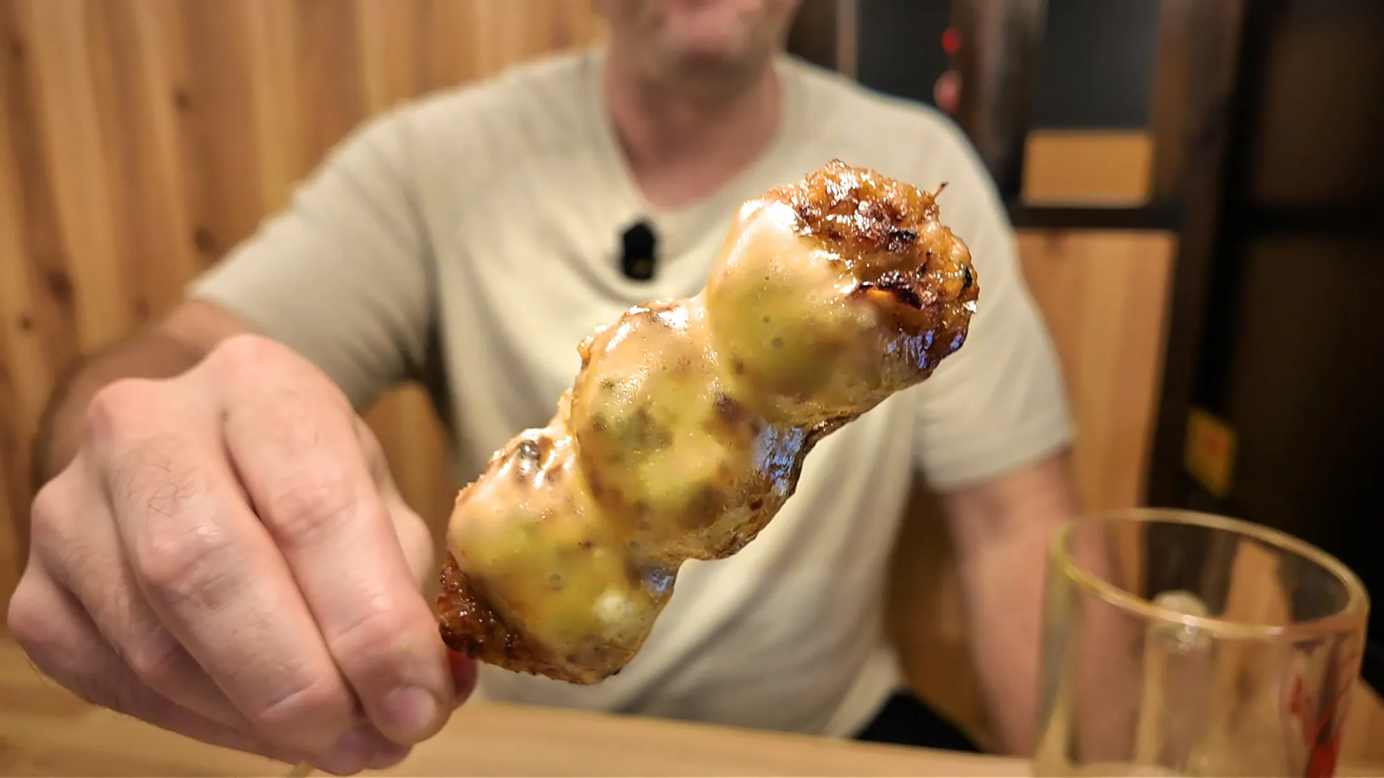 A chicken meatball skewer covered in melted cheese held up at Torikizoku in Tokyo