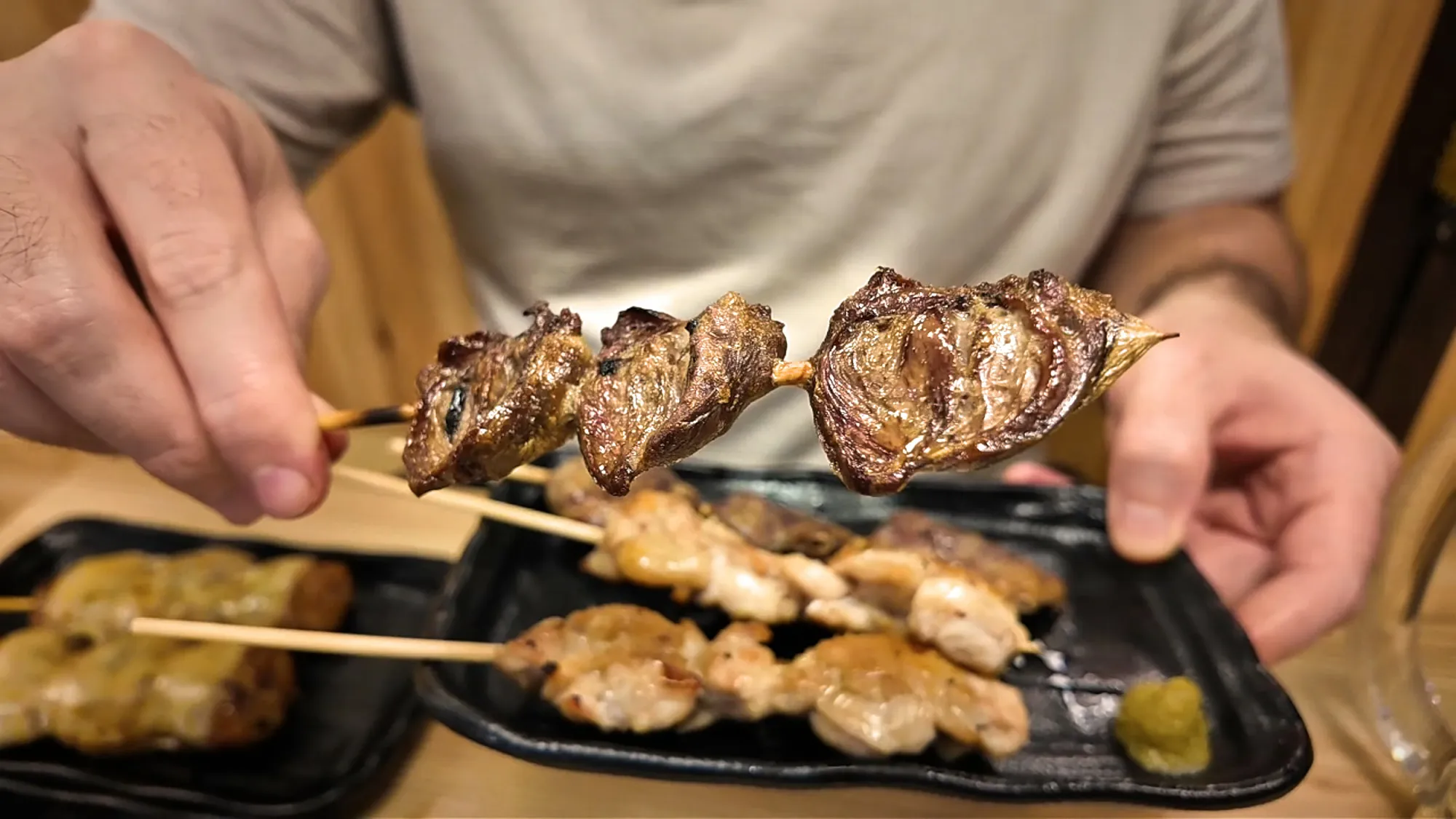 Grilled, sauced chicken heart skewers held over a plate at Torikizoku in Tokyo