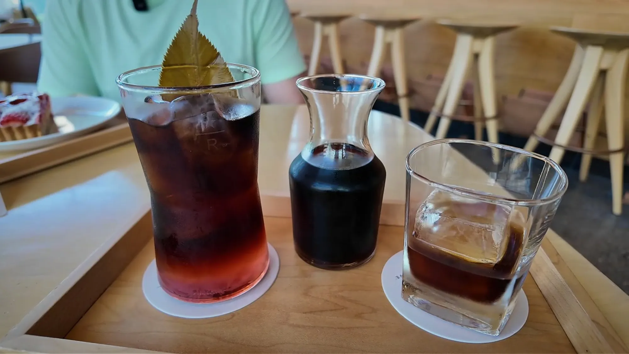 The Sakura barrel-aged cold brew with a leaf garnish next to the classic barrel-aged cold brew and its carafe at Starbucks Reserve Roastery Tokyo.