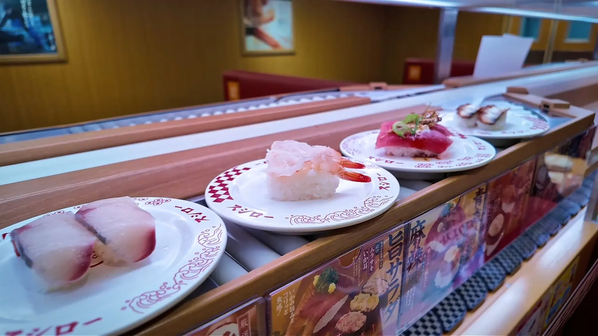 Plates of nigiri, including shrimp and seared tuna, riding the conveyor belt at Sushiro in Tokyo.