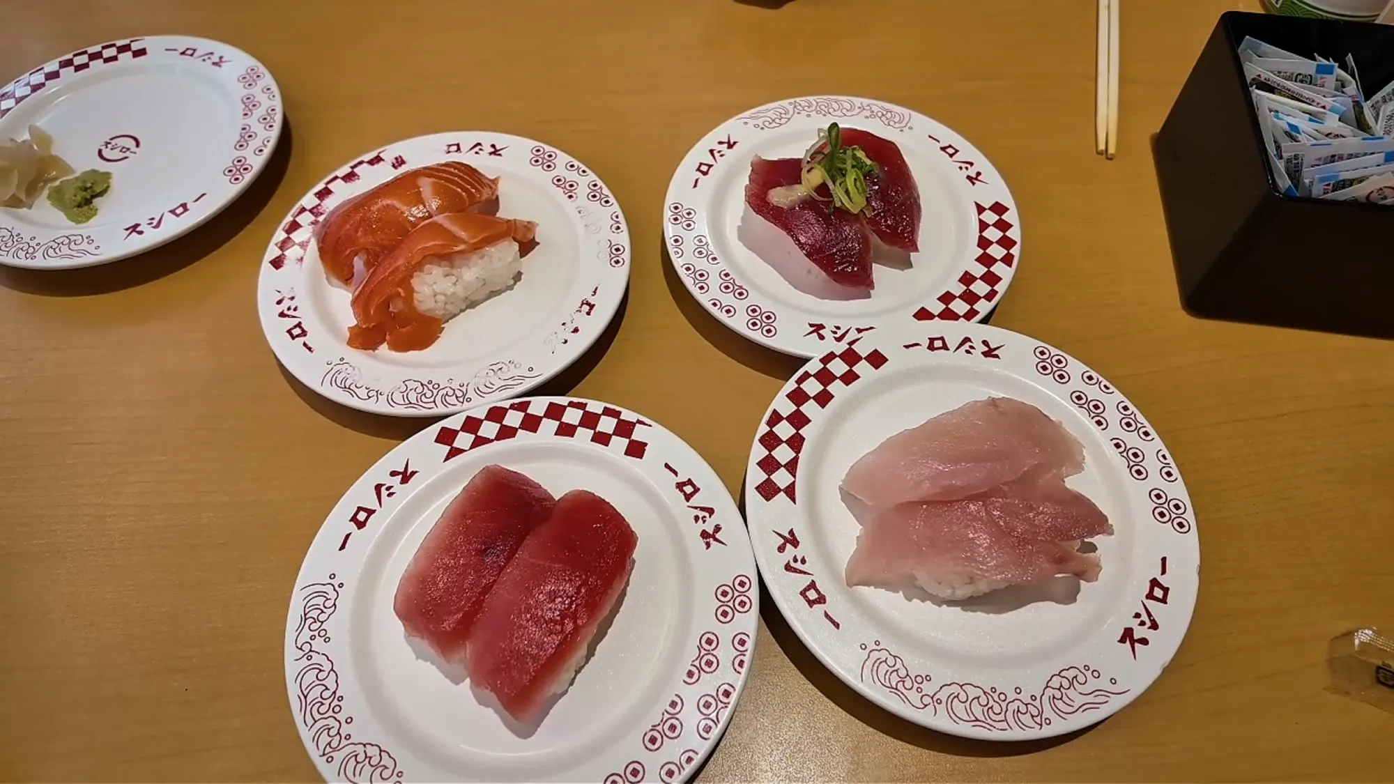 Four plates of nigiri on red-and-white Sushiro plates in Tokyo, with salmon, tuna, negitoro, and yellowtail.