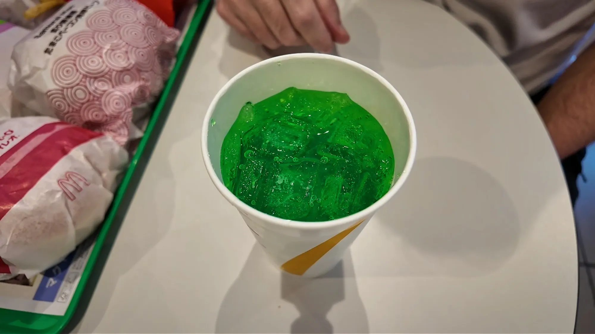 A cup of bright green Fanta Melon soda on a tray at McDonald's in Japan.