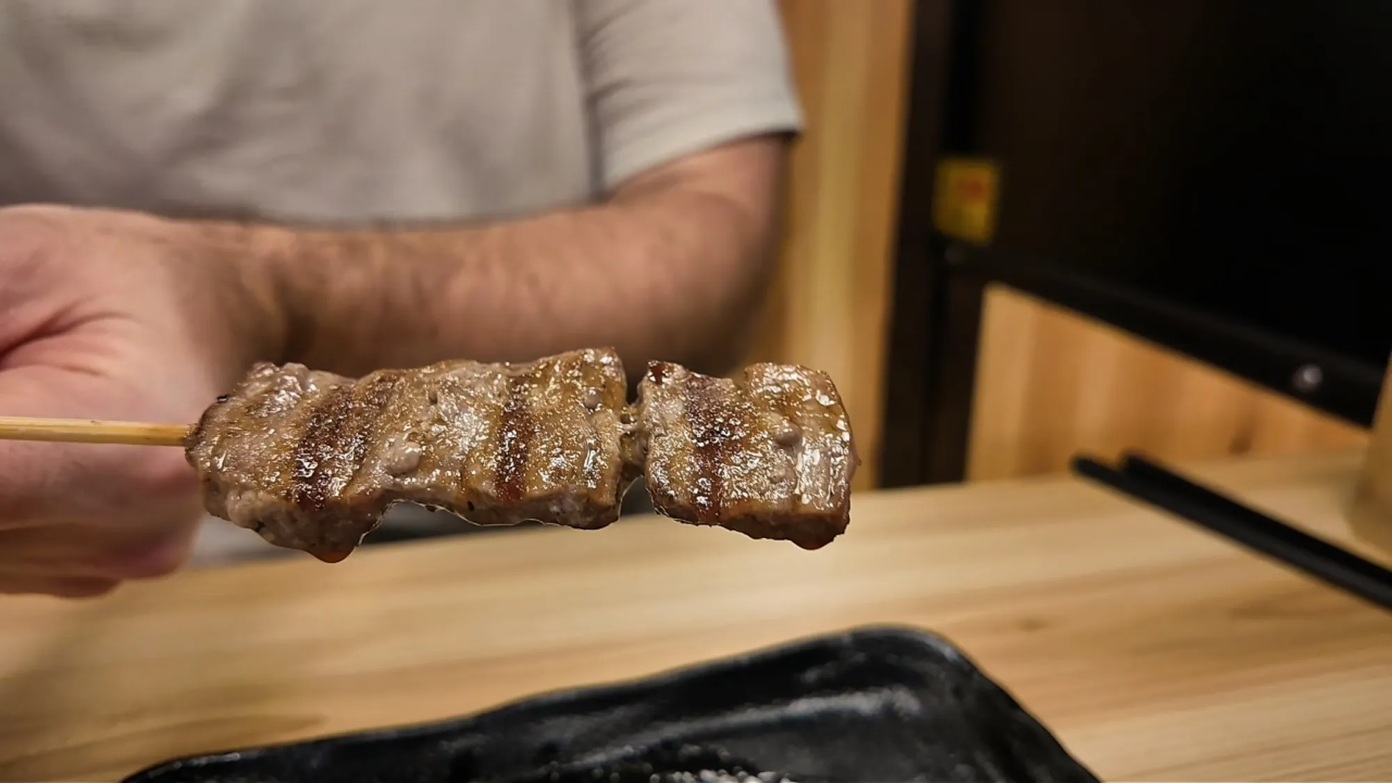 A grilled beef skewer held up at a wooden table at Torikizoku in Tokyo.