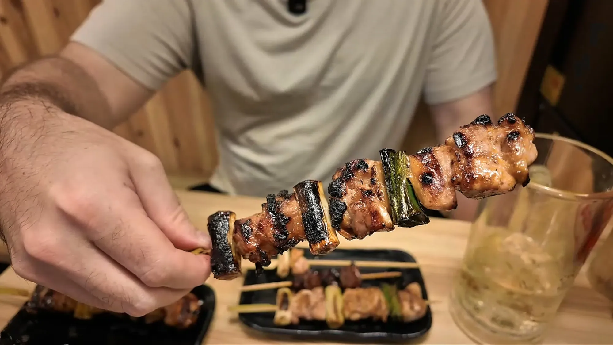 Holding up a sauced chicken thigh and leek yakitori skewer over the table at Torikizoku in Tokyo.