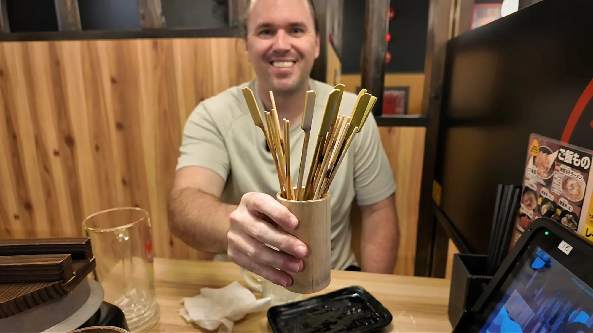 Cream smiling and holding up a wooden cup packed with empty yakitori skewers at the end of our meal at Torikizoku, Tokyo.