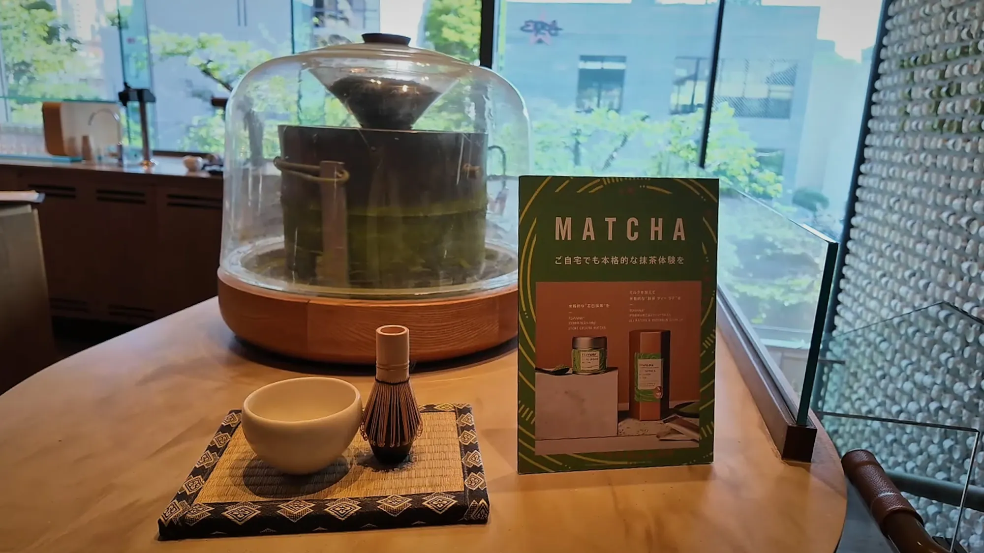 A stone matcha mill under a glass dome next to a matcha whisk and bowl on the Teavana floor of Starbucks Reserve Roastery Tokyo.