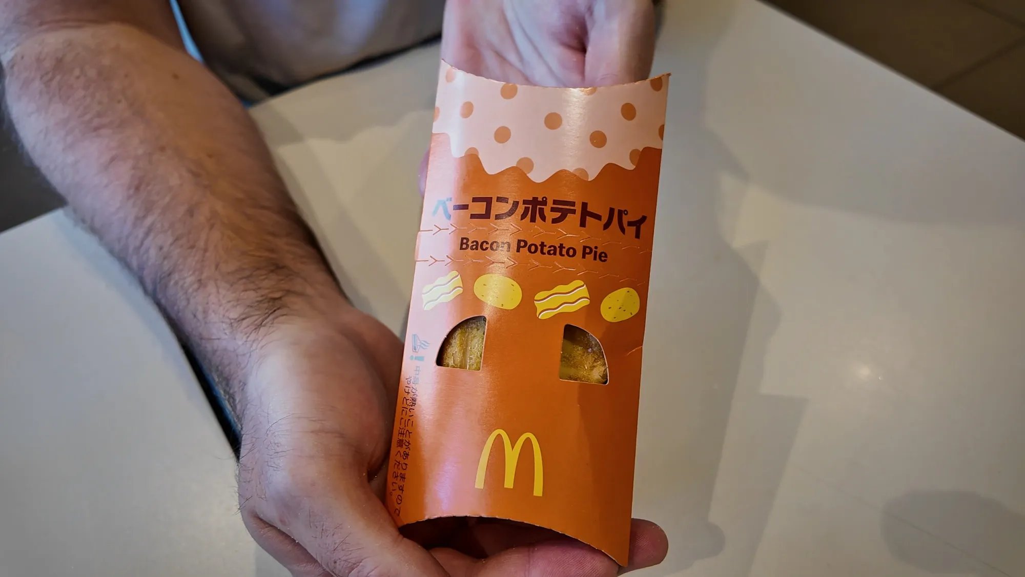 A Bacon Potato Pie in its orange sleeve at McDonald's in Japan, labeled in Japanese and English.