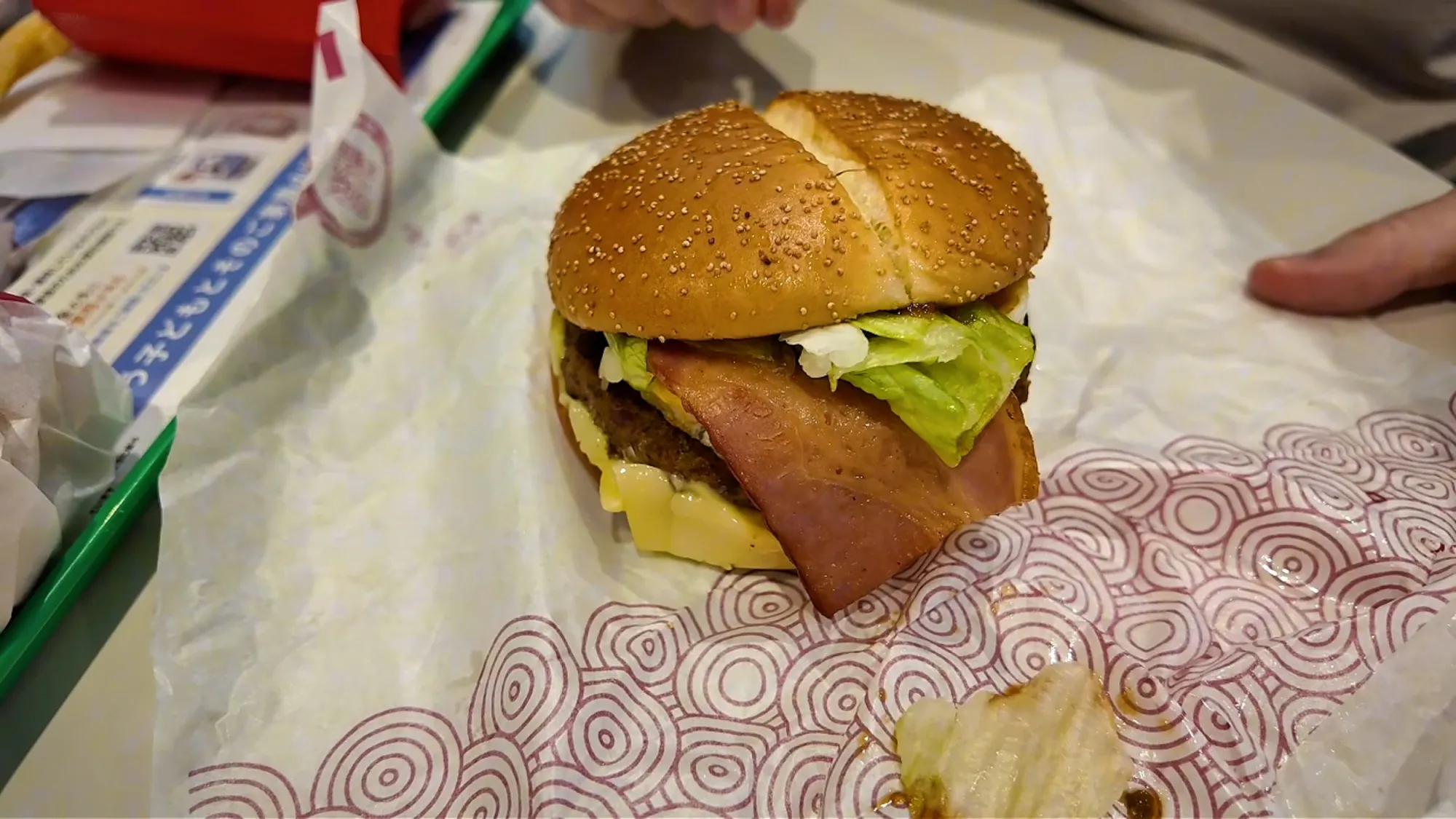 A Samurai Mac at McDonald's in Japan, opened on its wrapper to show the thick beef patty, bacon, egg, lettuce, and cheese in a sesame bun.