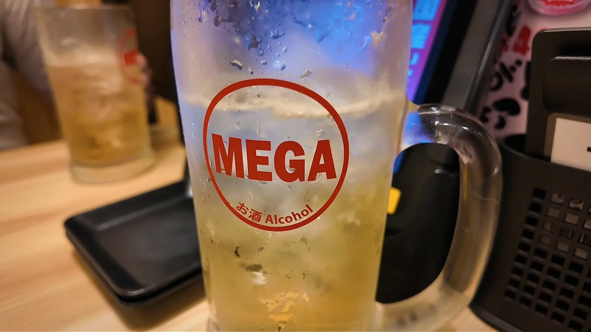 A huge frosted glass mug of mega highball with a red MEGA logo on a Torikizoku table in Tokyo.
