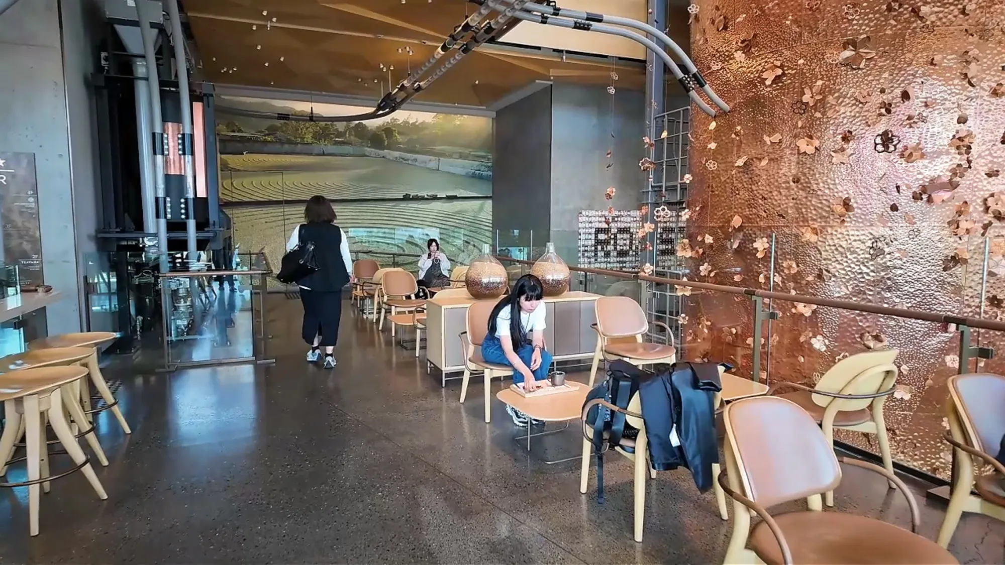 The first floor of Starbucks Reserve Roastery Tokyo, with wooden tables and chairs in front of the copper cask and copper pipes overhead.