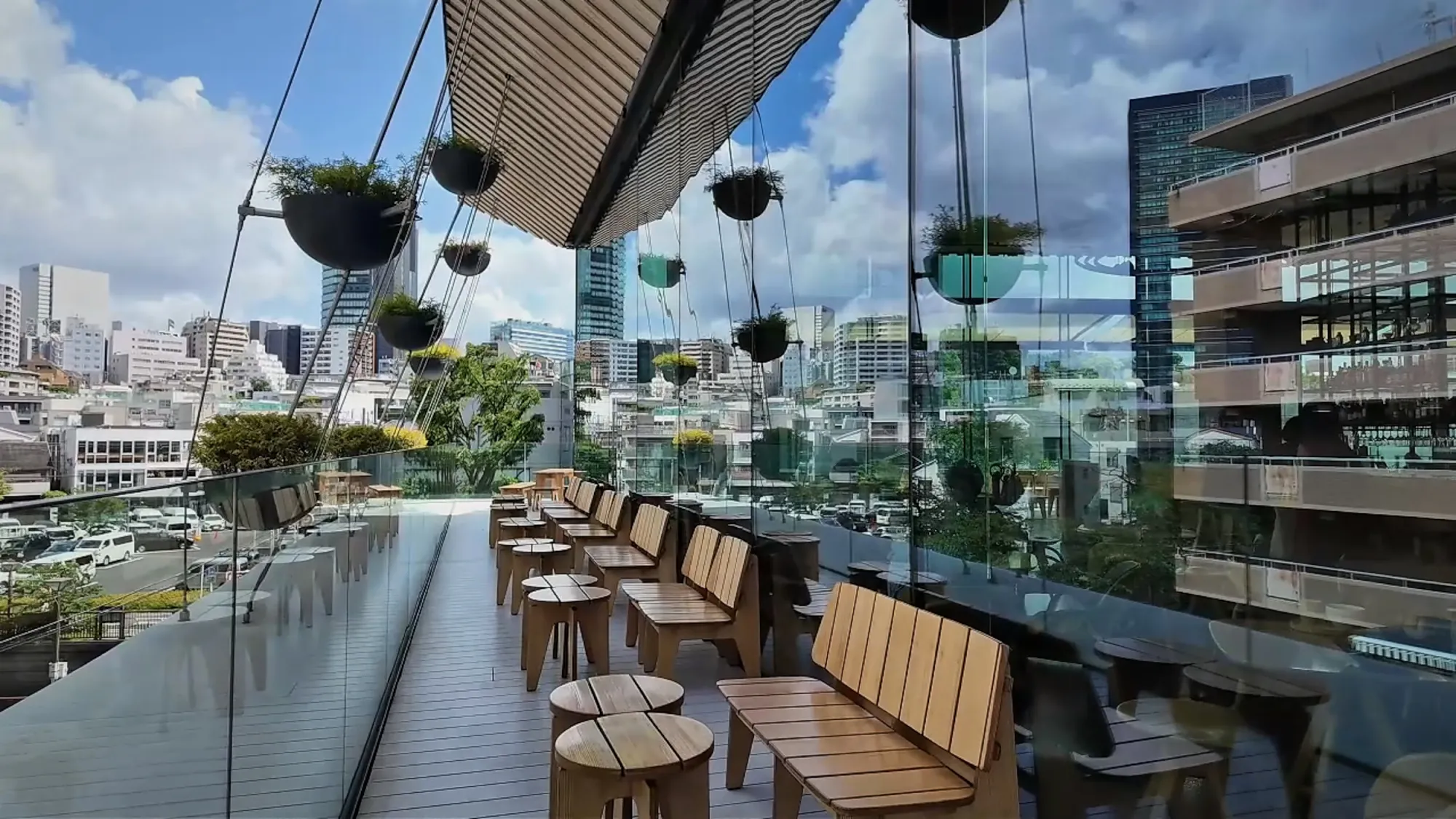 The rooftop terrace at the Starbucks Reserve Roastery in Nakameguro, with wooden benches, hanging plants, and a glass railing looking out over the neighborhood.