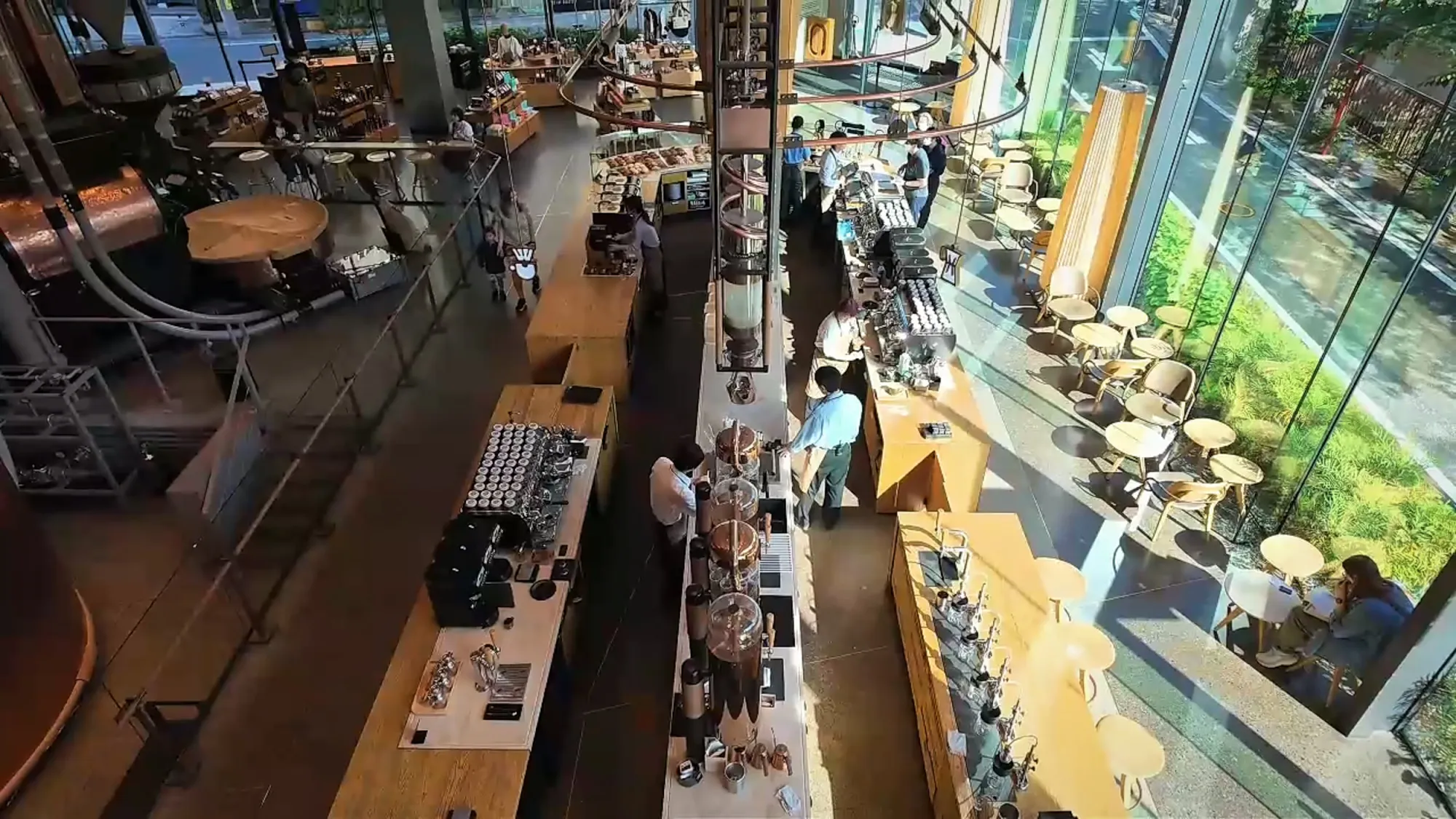 Looking down from an upper floor onto the coffee bar and tables of Starbucks Reserve Roastery Tokyo, with trees outside the windows.