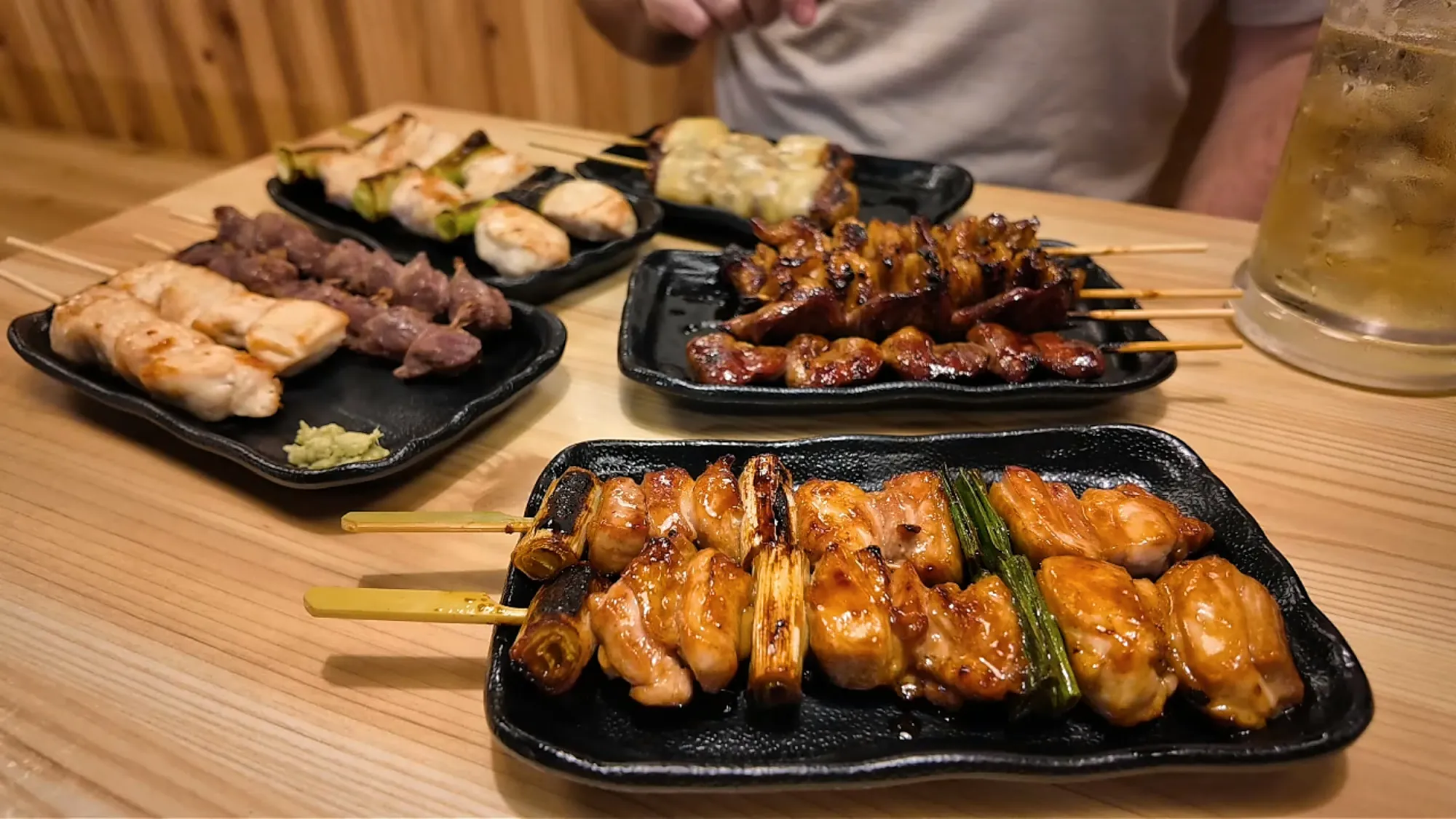 Several black plates of grilled yakitori skewers on a wooden table at Torikizoku in Tokyo.