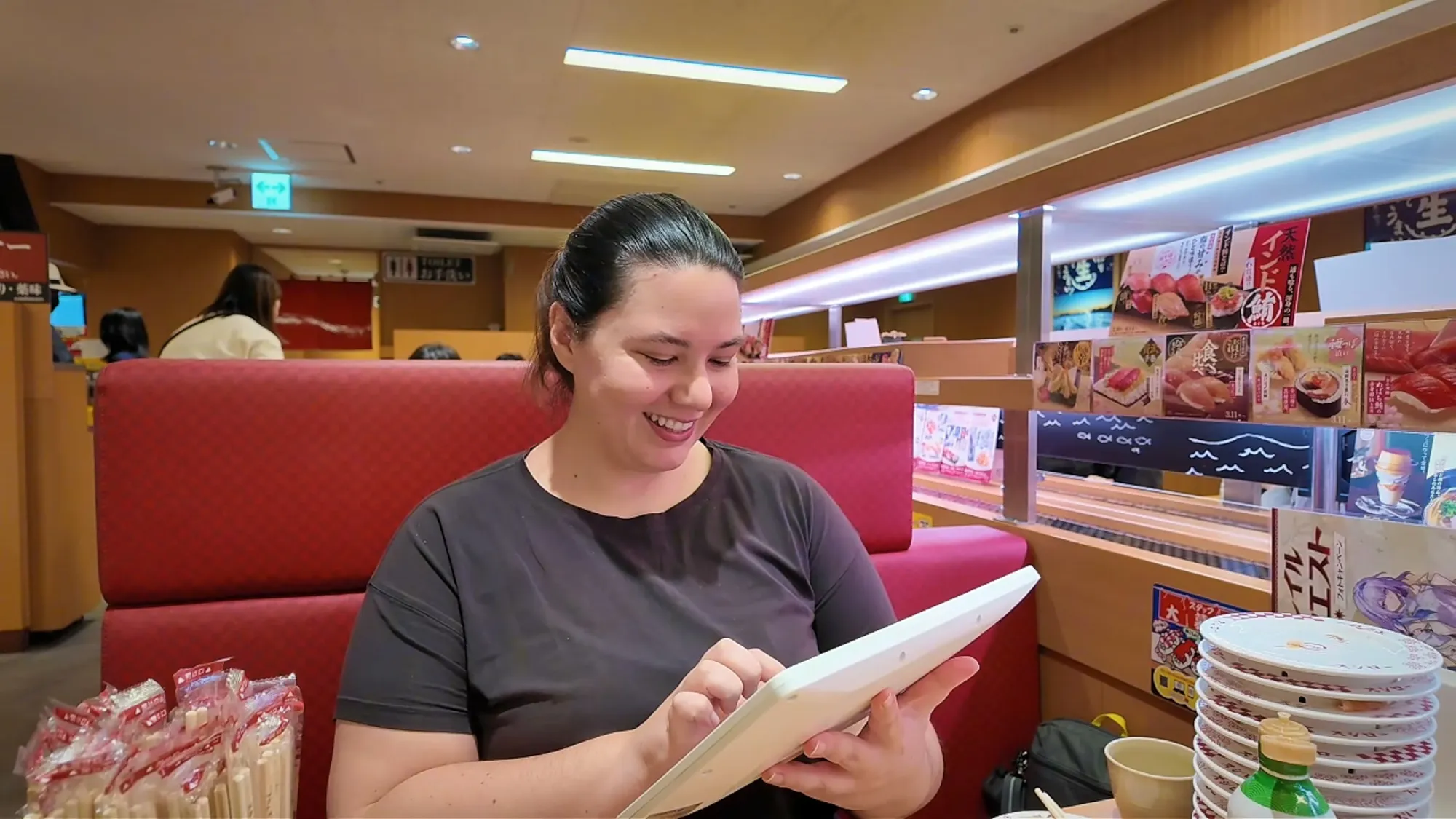Bernie smiling as she taps an order into the tablet at a Sushiro booth in Tokyo.