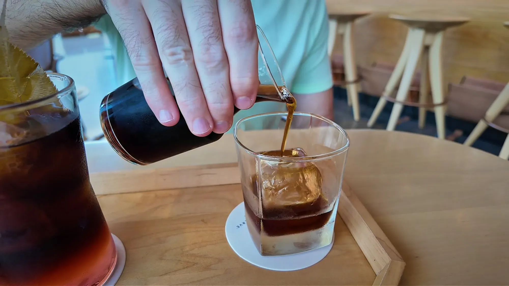 Pouring barrel-aged cold brew from a small carafe over a large ice cube in a rocks glass at Starbucks Reserve Roastery Tokyo.