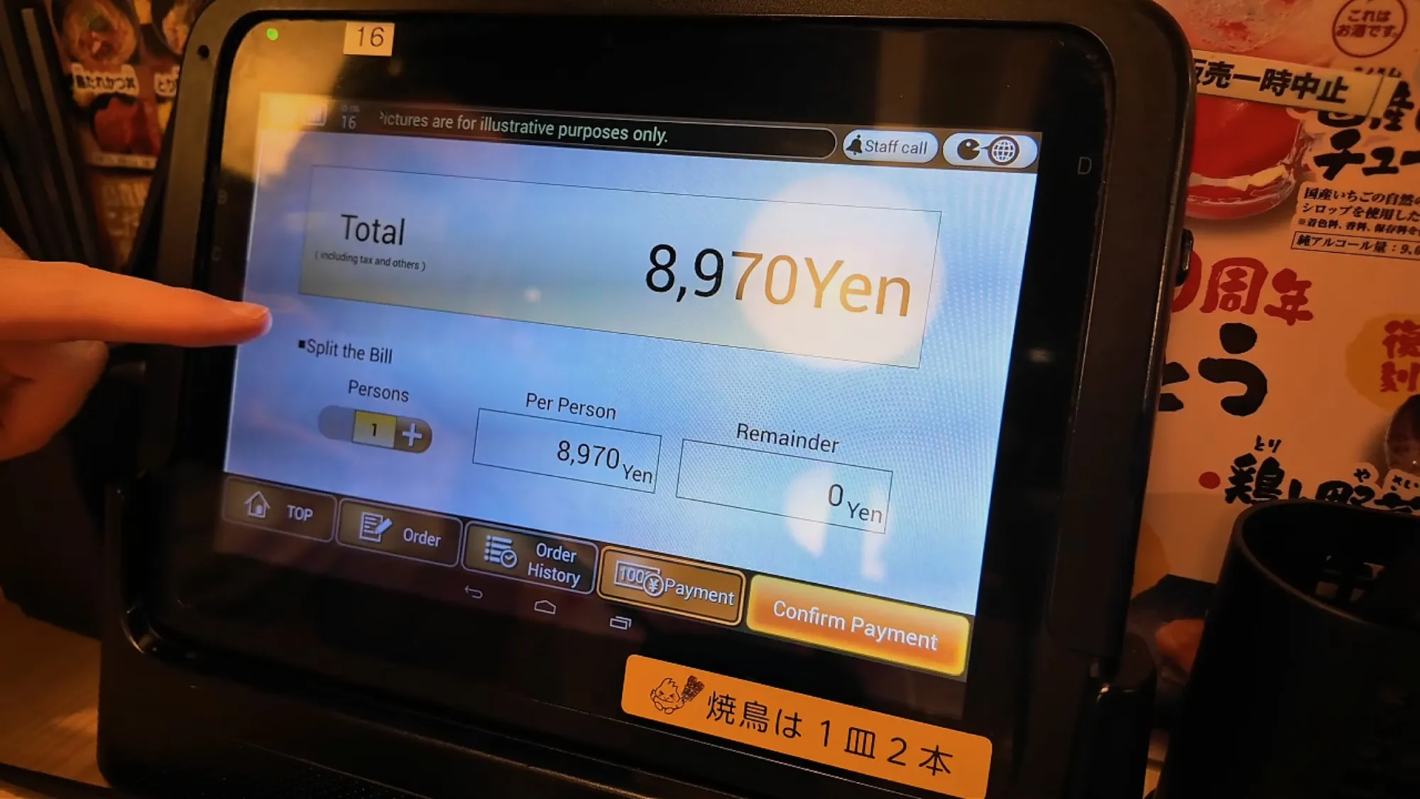 A finger pointing at a table tablet at Torikizoku in Tokyo showing an 8,970 yen total and a split-the-bill option.