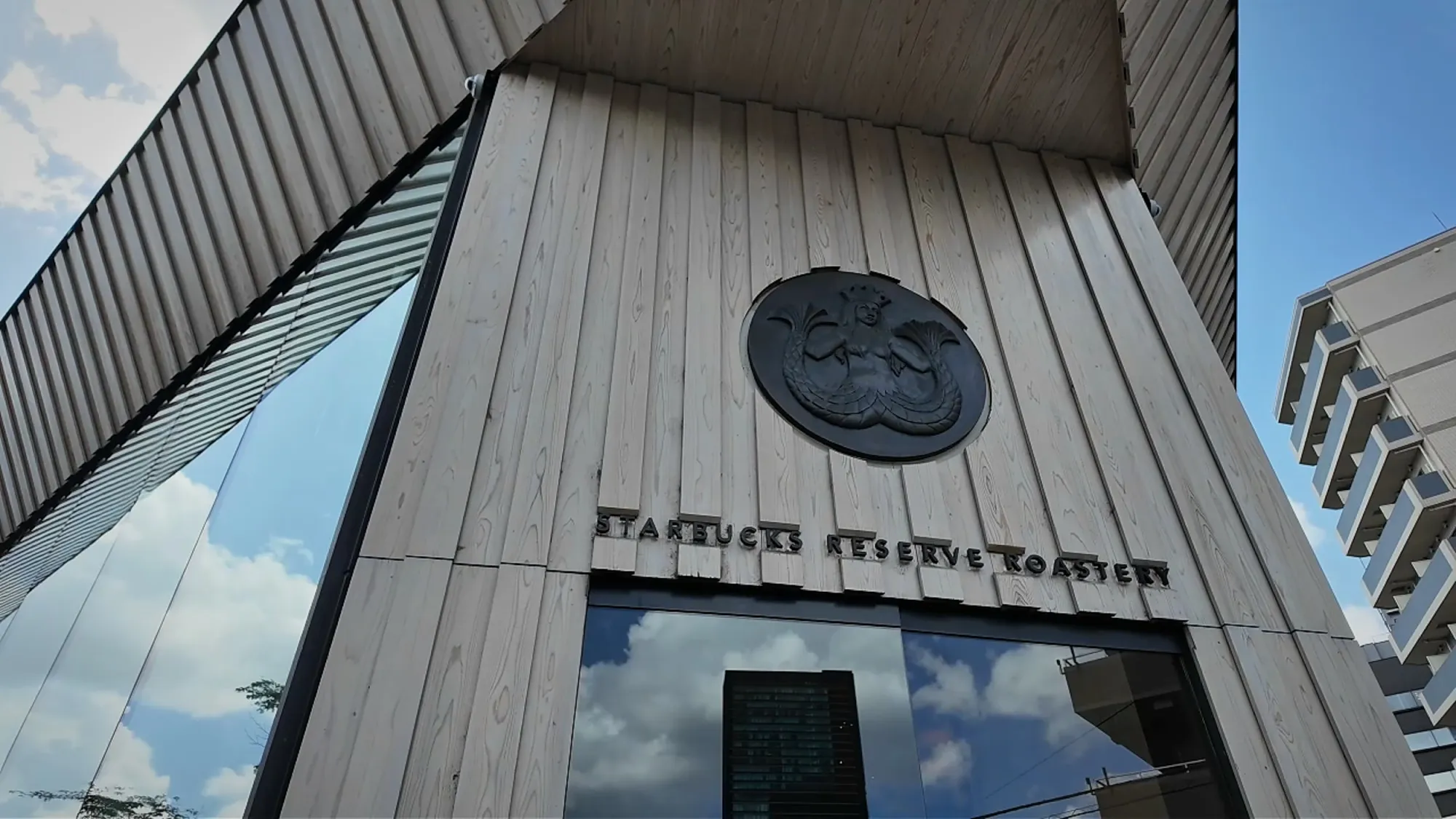 Looking up at the wooden entrance of Starbucks Reserve Roastery Tokyo with the round siren logo above the doors.