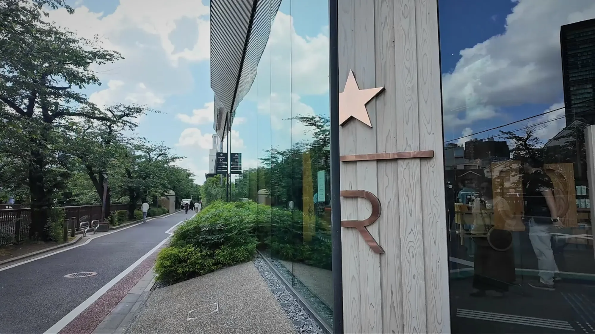 The copper star and R of the Starbucks Reserve sign on the wooden facade, with the tree-lined path along the Meguro River behind.