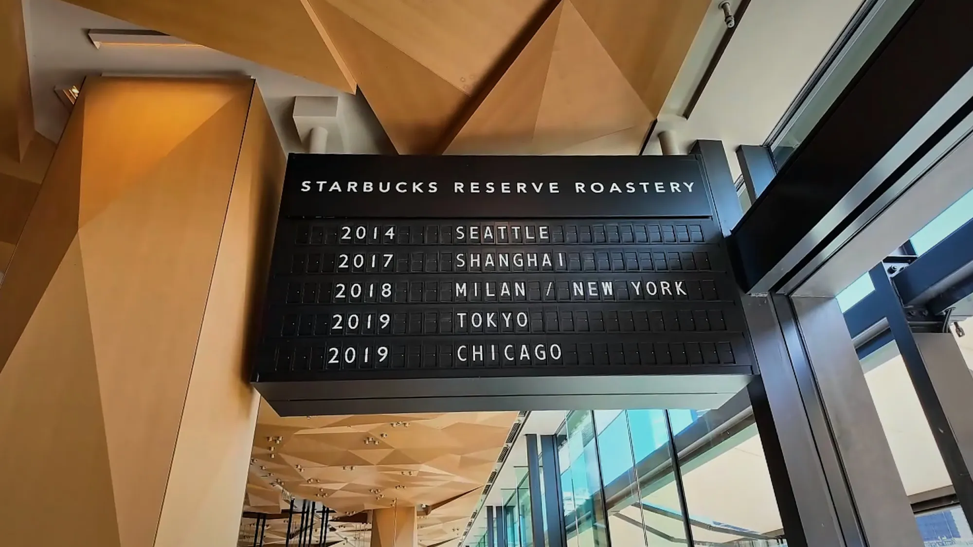 A black board inside Starbucks Reserve Roastery Tokyo listing the Roasteries by year: Seattle 2014, Shanghai 2017, Milan and New York 2018, Tokyo and Chicago 2019.