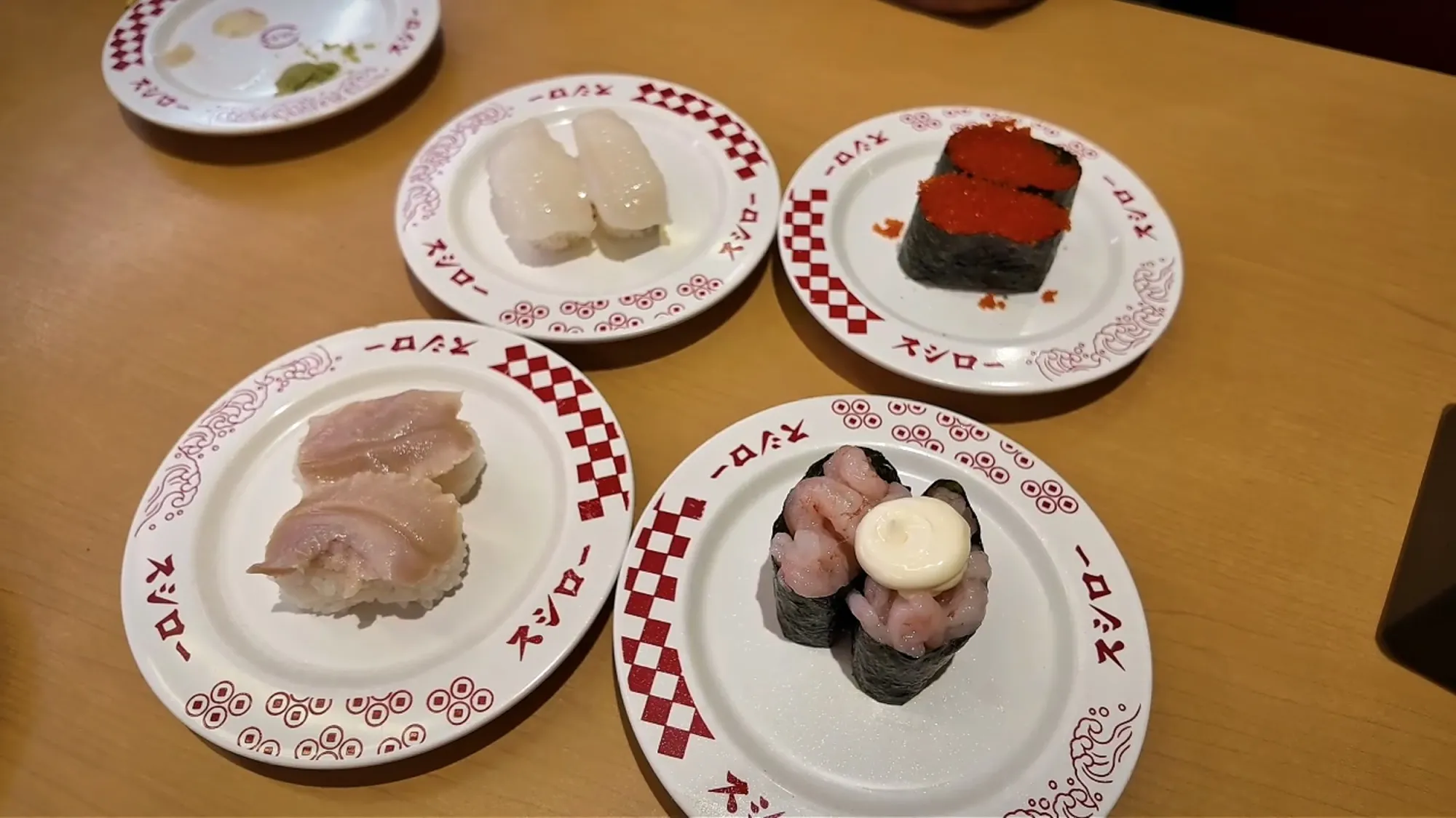 Four red-and-white Sushiro plates in Tokyo with squid, fish roe, white fish, and a mayonnaise-topped gunkan.