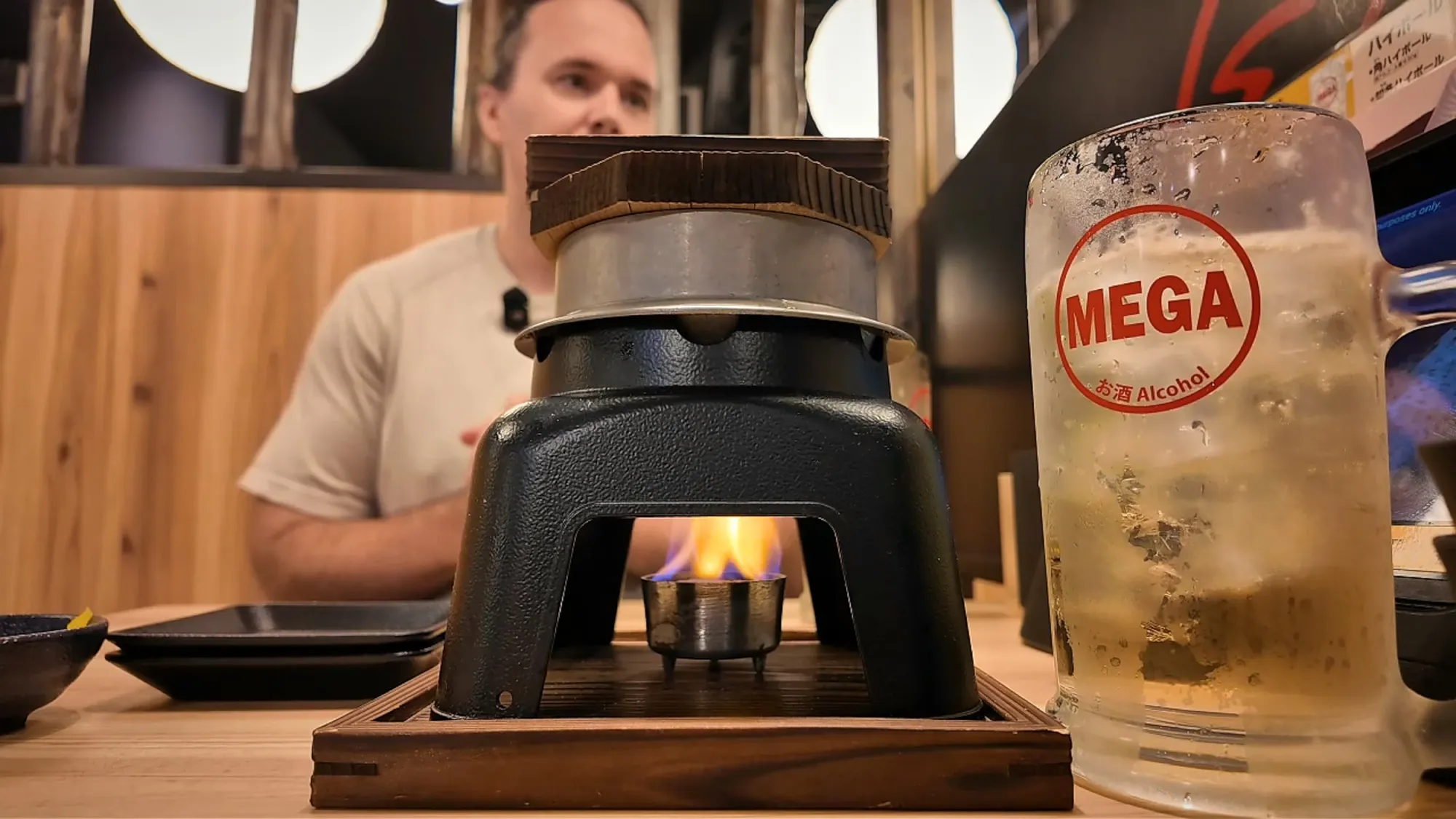 A small kamameshi rice pot cooking over a lit tabletop burner next to a mega highball at Torikizoku, Tokyo.