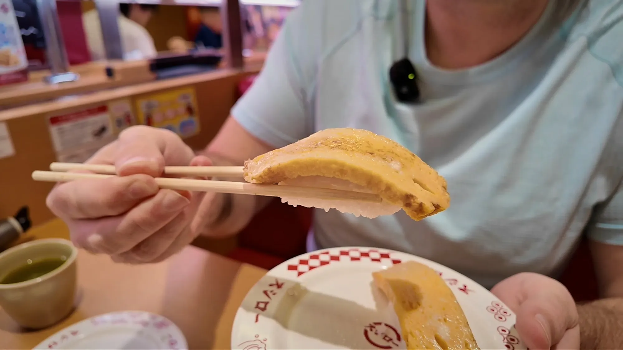 Chopsticks holding a slab of tamago egg nigiri at Sushiro in Tokyo.