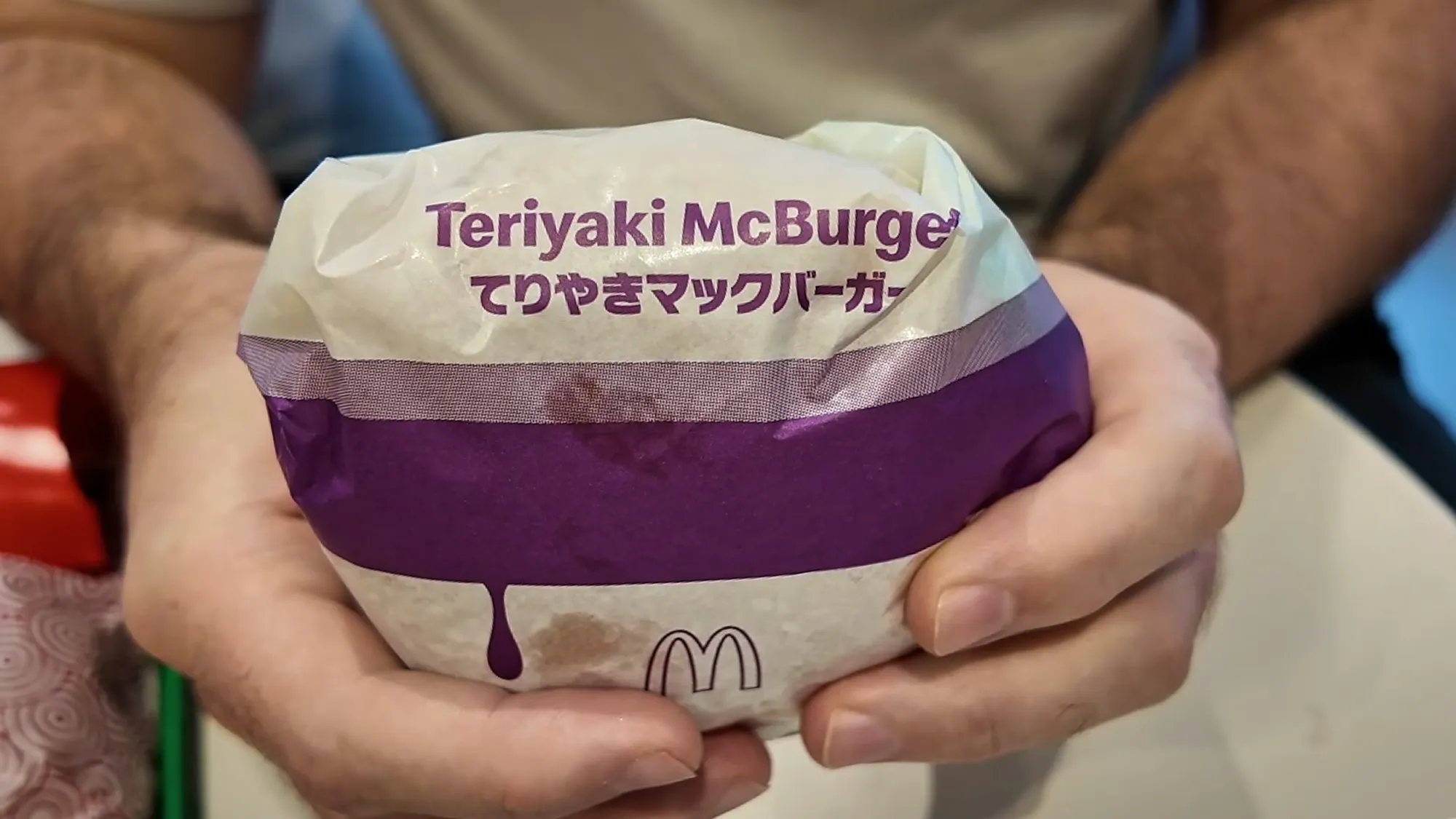 A Teriyaki McBurger in its purple and white wrapper, held over the table at McDonald's in Japan.