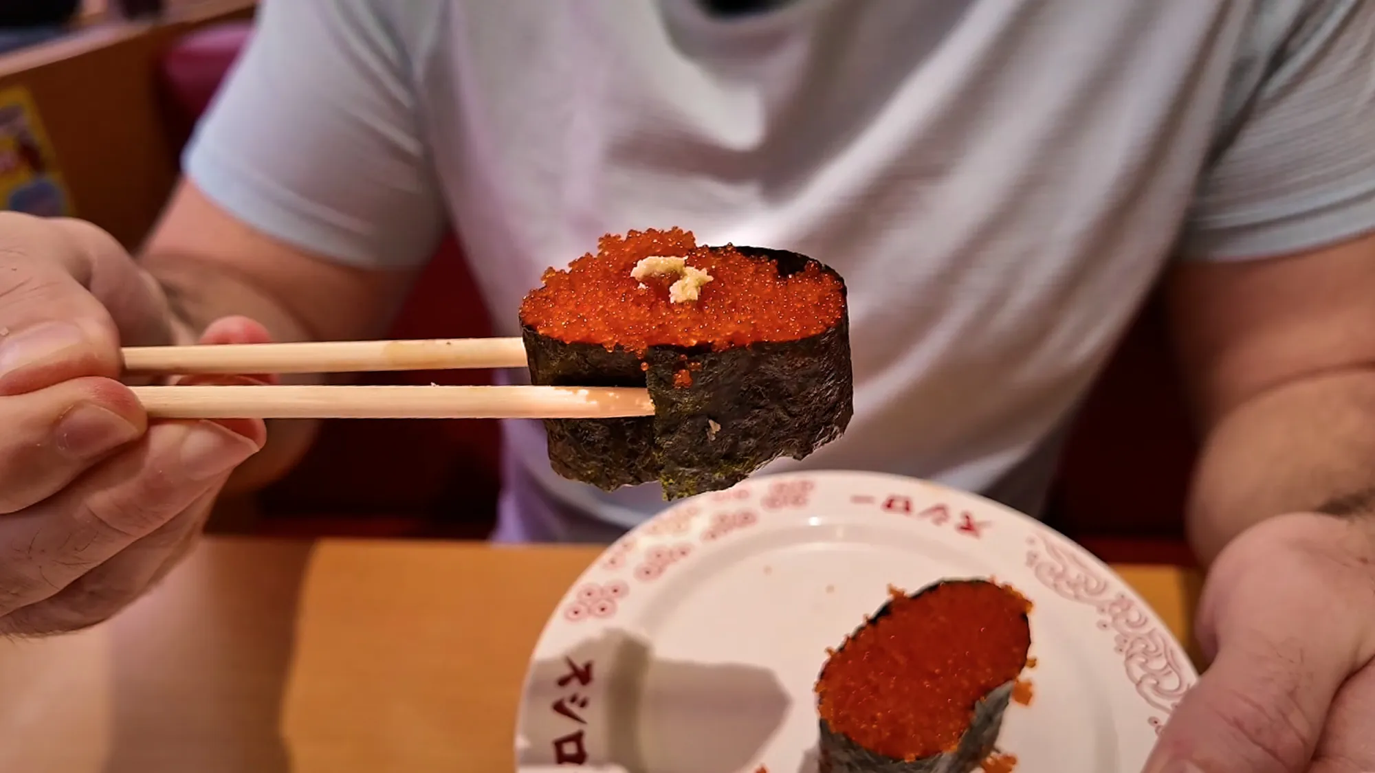 Chopsticks holding a gunkan of bright orange fish roe at Sushiro in Tokyo.