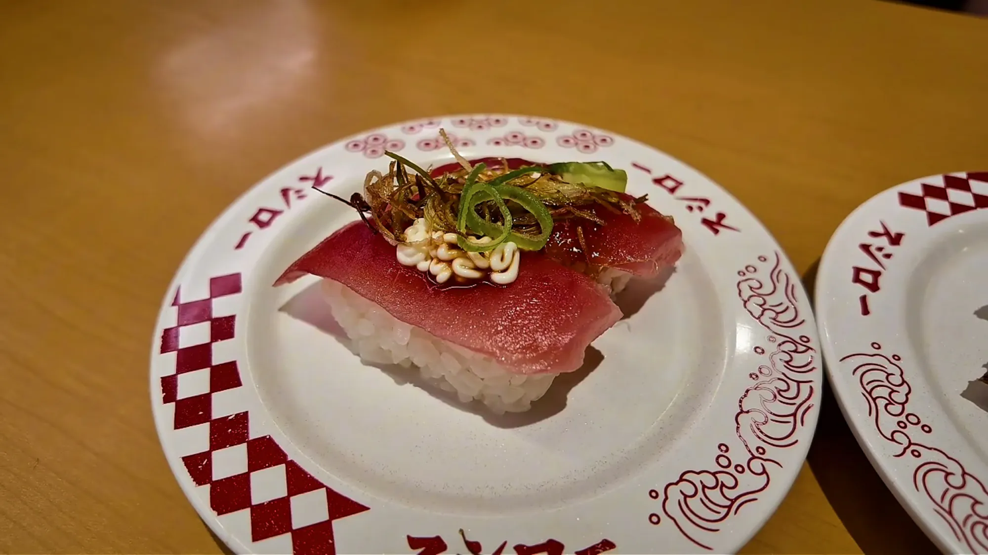 A close-up of tuna nigiri topped with green onion on a Sushiro plate in Tokyo.