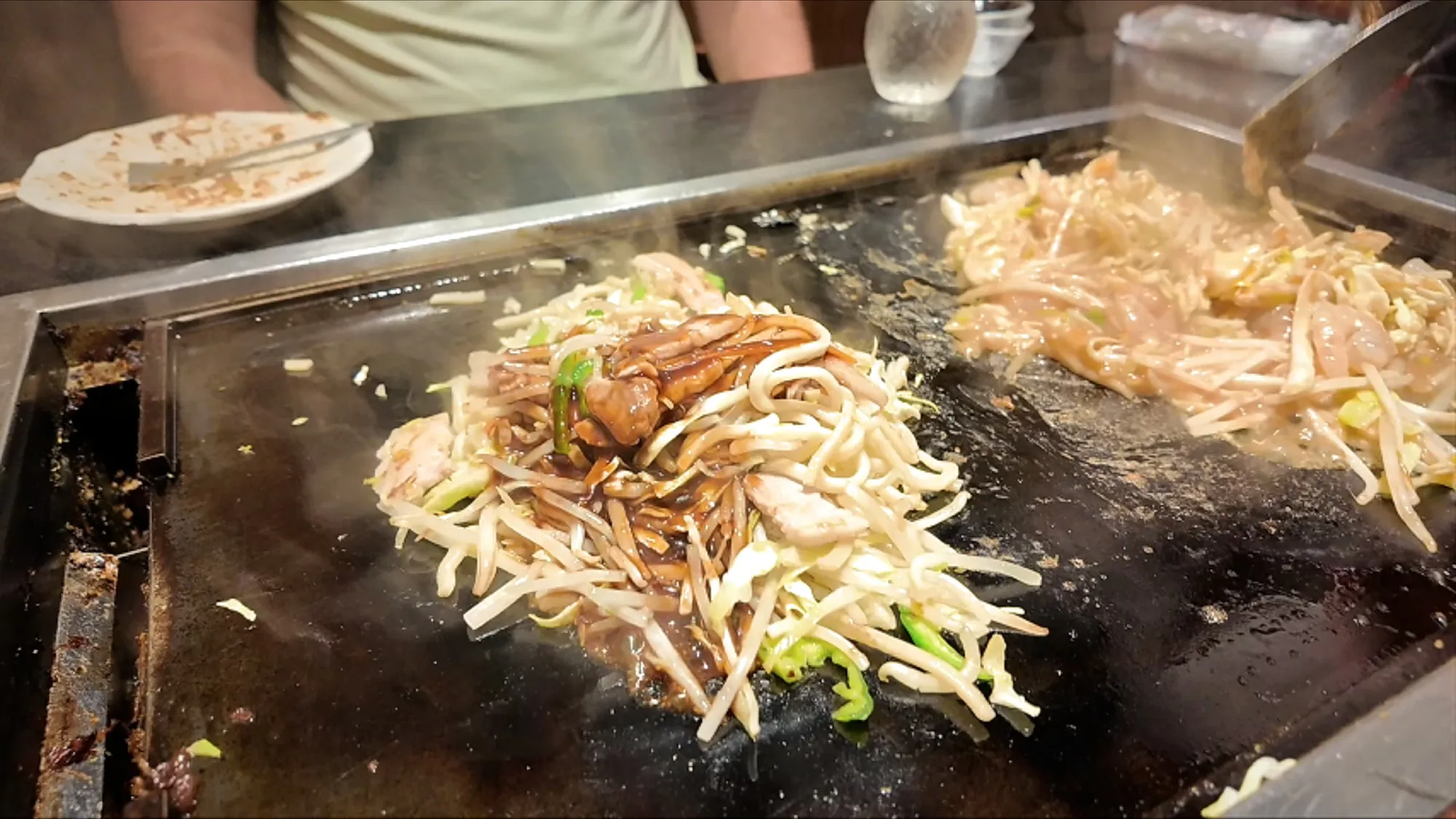 Pork yakisoba noodles with bean sprouts and cabbage cooking on the teppan griddle next to shrimp monjayaki at Osakaya, Tokyo.
