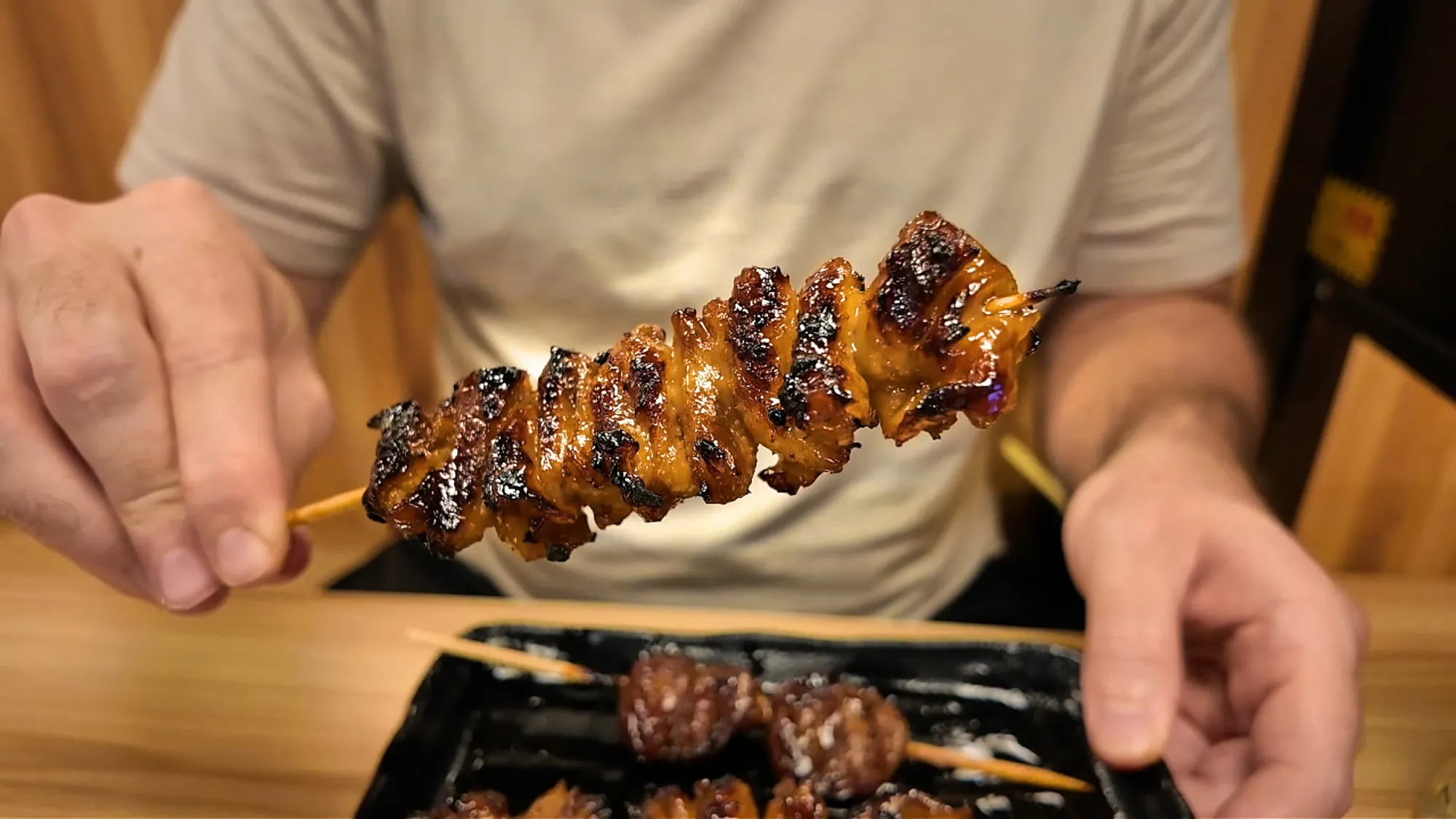 A sauced, crispy chicken skin skewer held up over the table at Torikizoku, Tokyo.