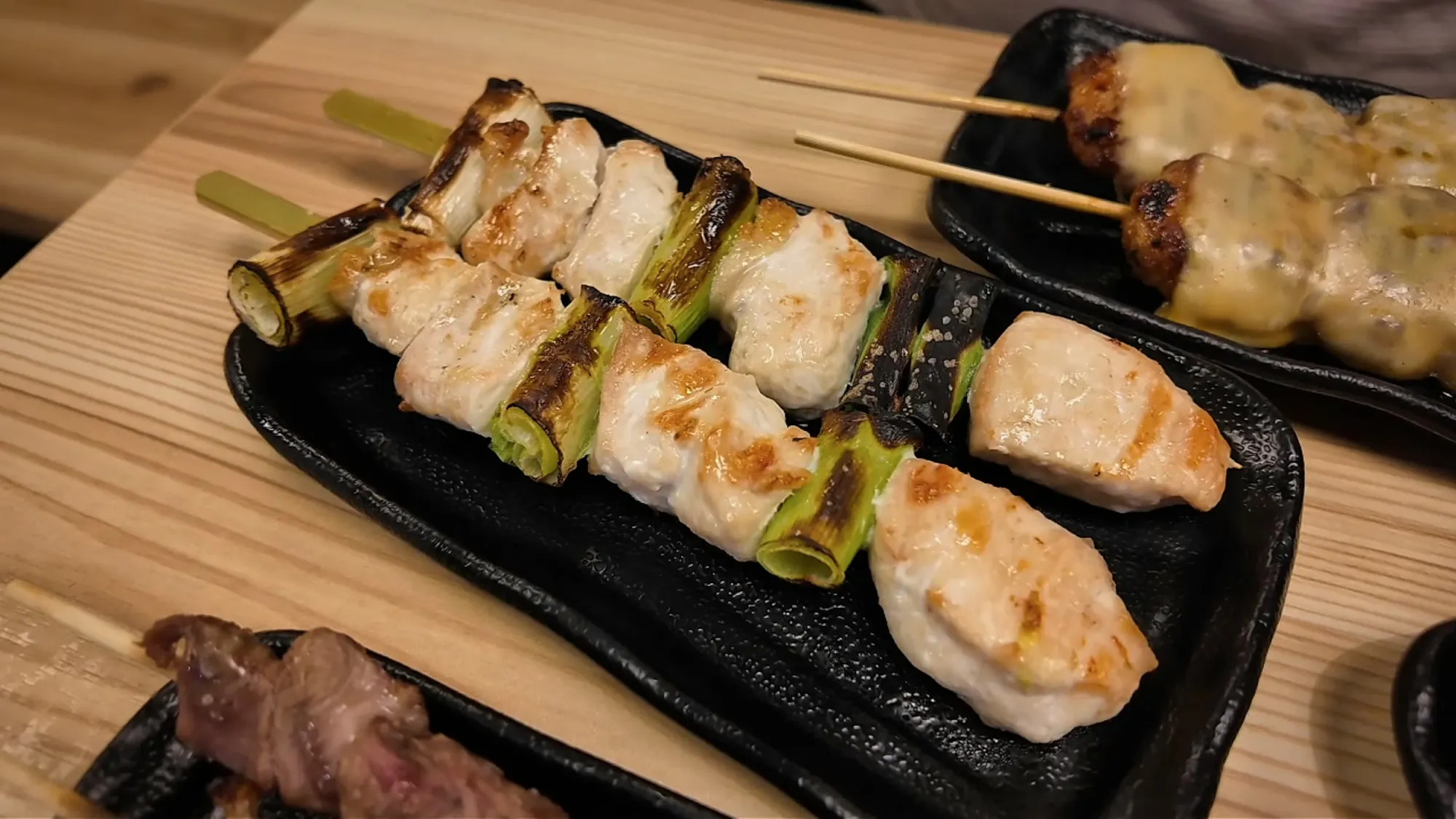 Salted chicken breast and leek yakitori skewers on a black plate at Torikizoku in Tokyo.