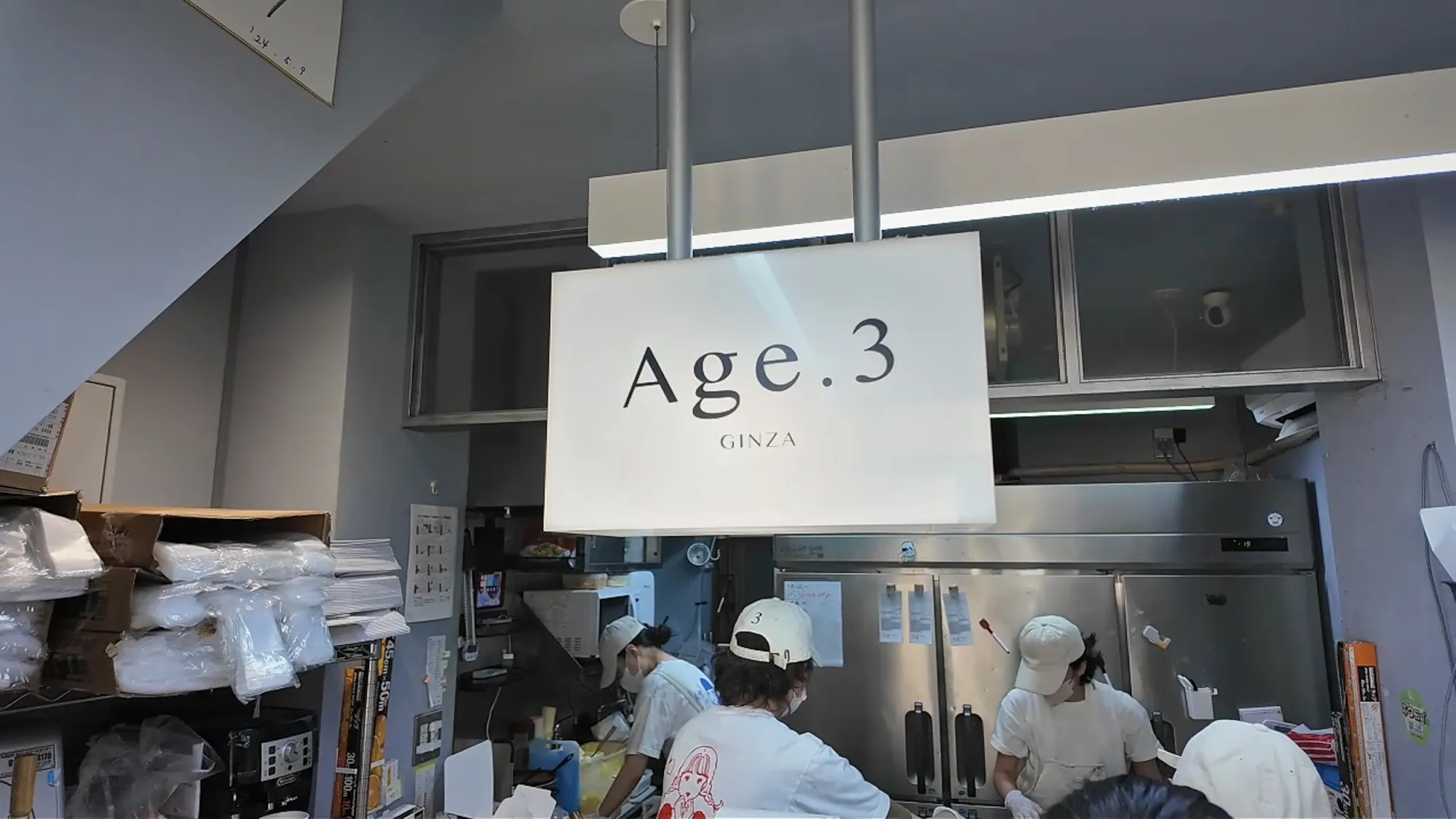 The white Age.3 GINZA sign hanging over the small open shopfront and kitchen in Ginza, Tokyo.
