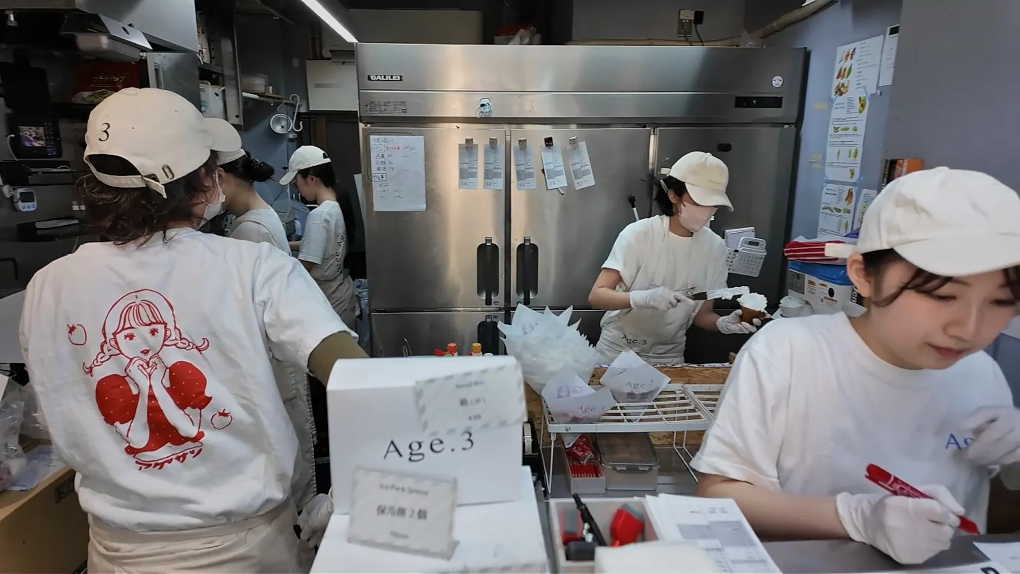 Staff in white caps and Age.3 T-shirts packing fried sandwiches behind the counter at Age.3 Ginza.