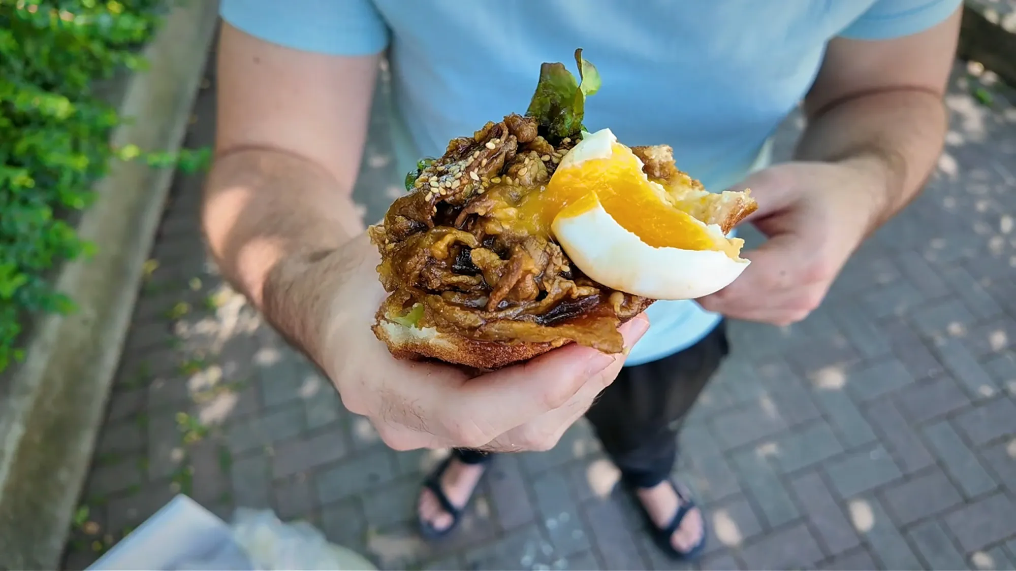 The Age.3 beef short rib yakiniku sandwich held up with its soft-boiled egg and sauced beef spilling over the top.