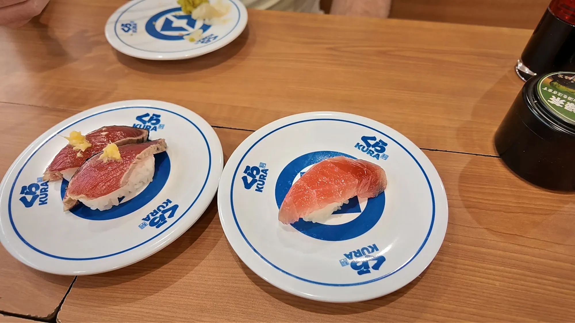 Bonito tataki and tuna nigiri on blue-and-white Kura Sushi plates in Tokyo.