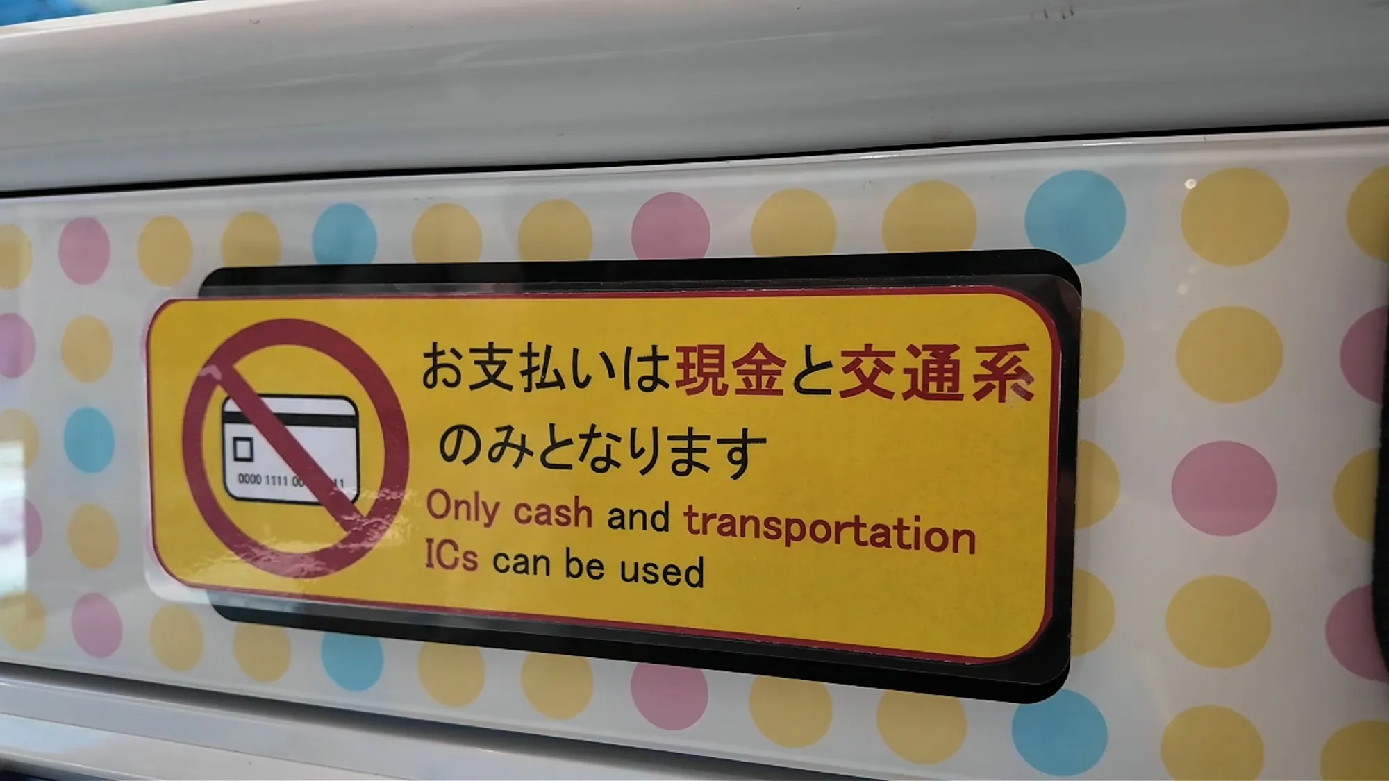 A yellow sign on a restaurant kiosk in Tokyo reading "Only cash and transportation ICs can be used" in Japanese and English, with a crossed-out credit card.