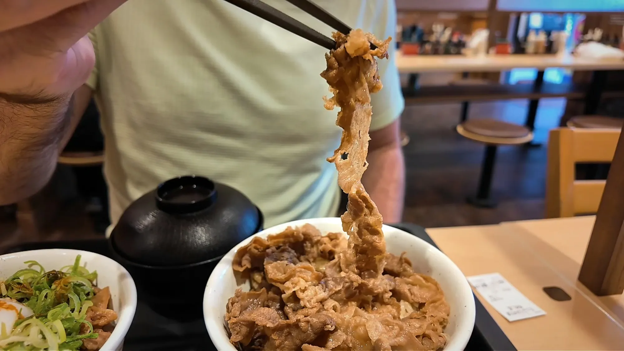 Chopsticks lifting slices of simmered beef and onion out of a gyudon bowl at Matsuya in Tokyo.