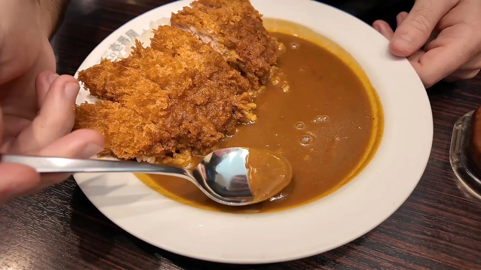 A plate of pork cutlet curry with rice at CoCo Ichibanya in Tokyo, with a spoon lifting some curry.