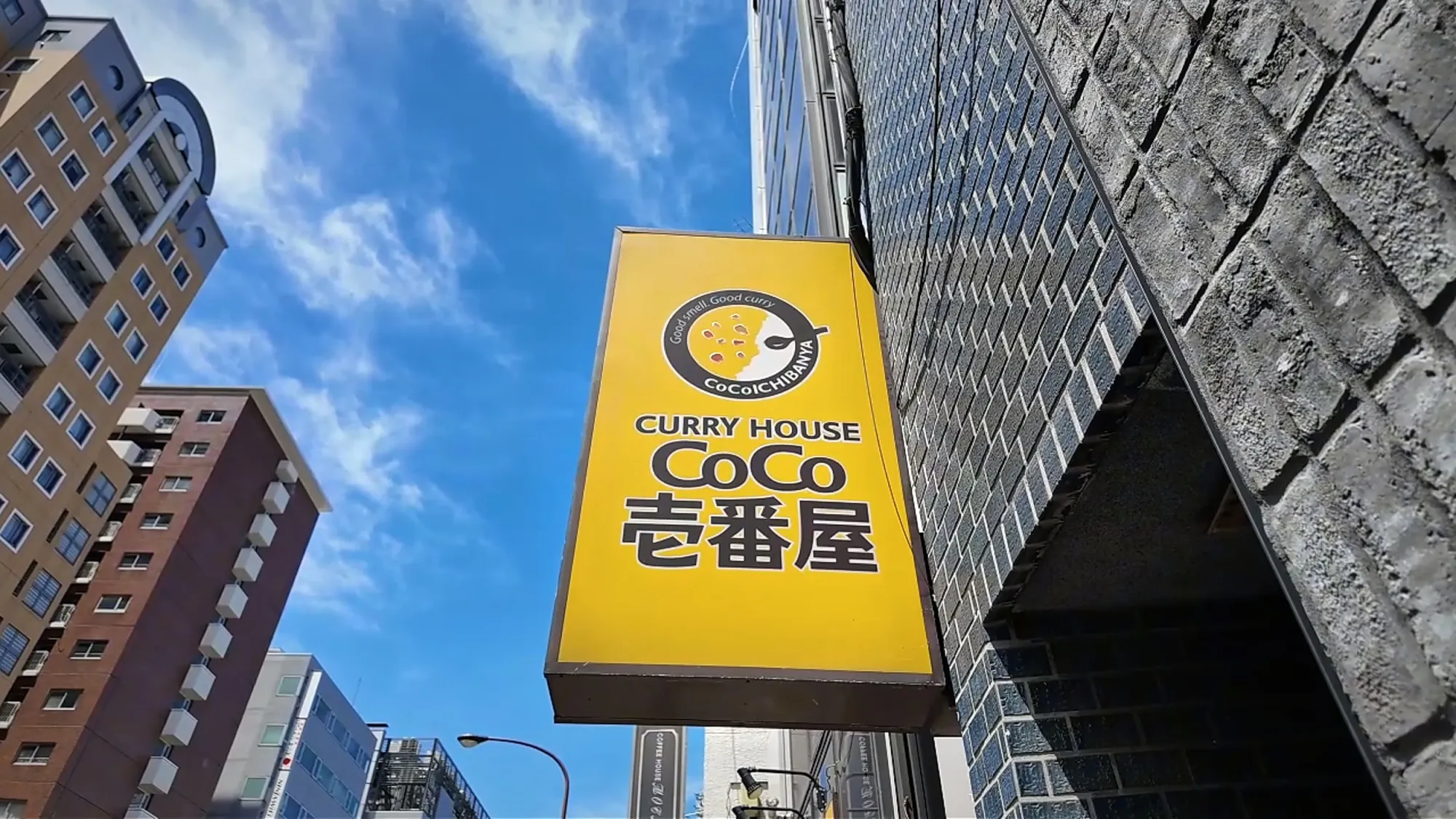 The yellow Curry House CoCo Ichibanya sign against a blue sky in Shinjuku